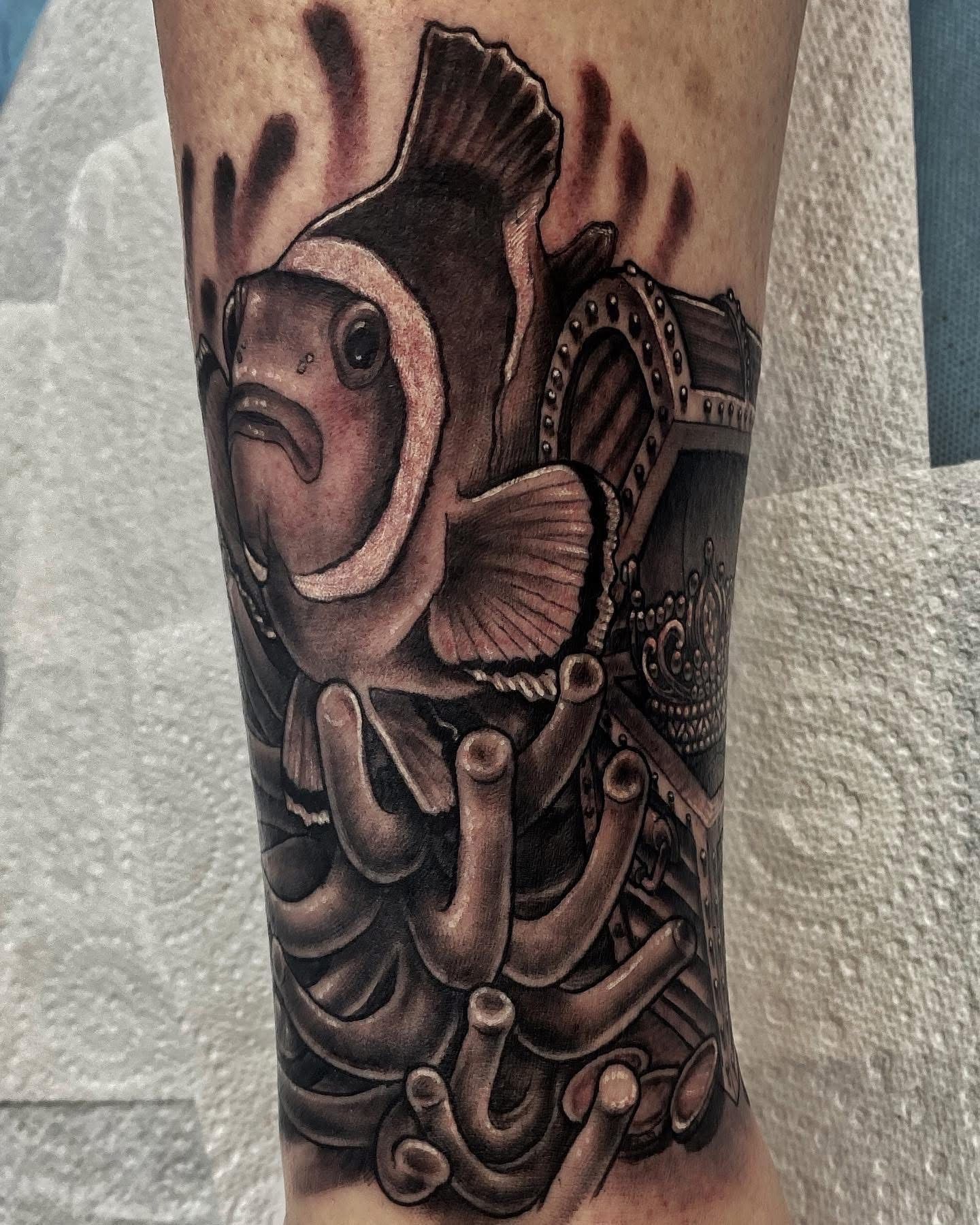 Tattoo of a clownfish, treasure chest, and coral on an arm in black and gray. — Whitsunday Tattooing Airlie Beach in Whitsundays, QLD