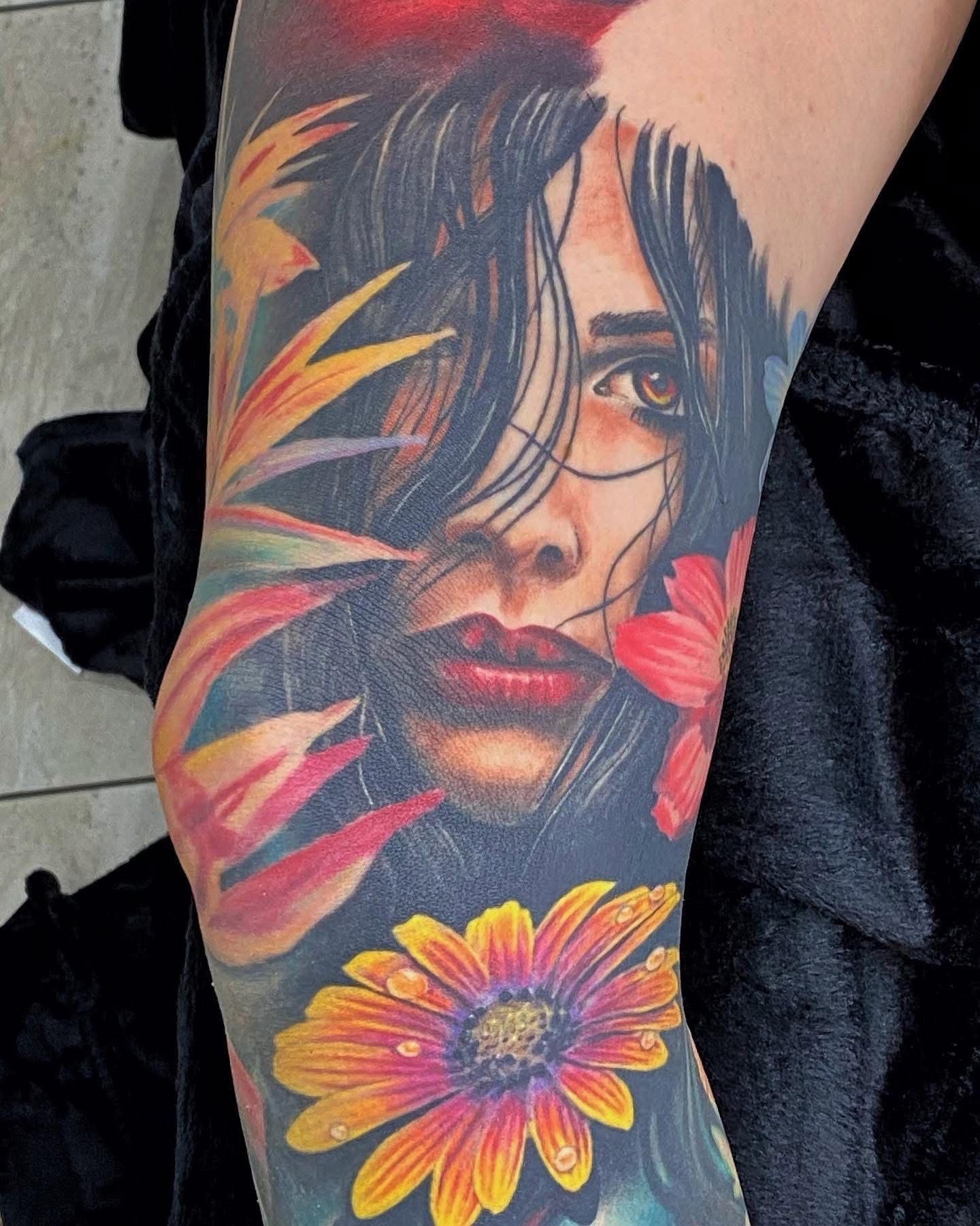 Tattoo of a woman's face surrounded by colorful flowers on an arm. — Whitsunday Tattooing Airlie Beach in Whitsundays, QLD