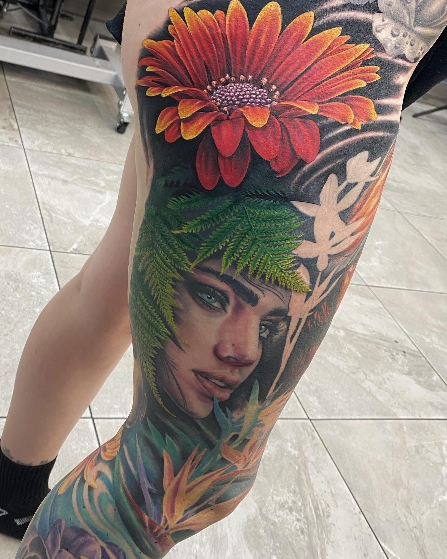 Leg tattoo featuring a vibrant orange flower, portrait, and botanical elements, in a tattoo studio. — Whitsunday Tattooing Airlie Beach in Whitsundays, QLD