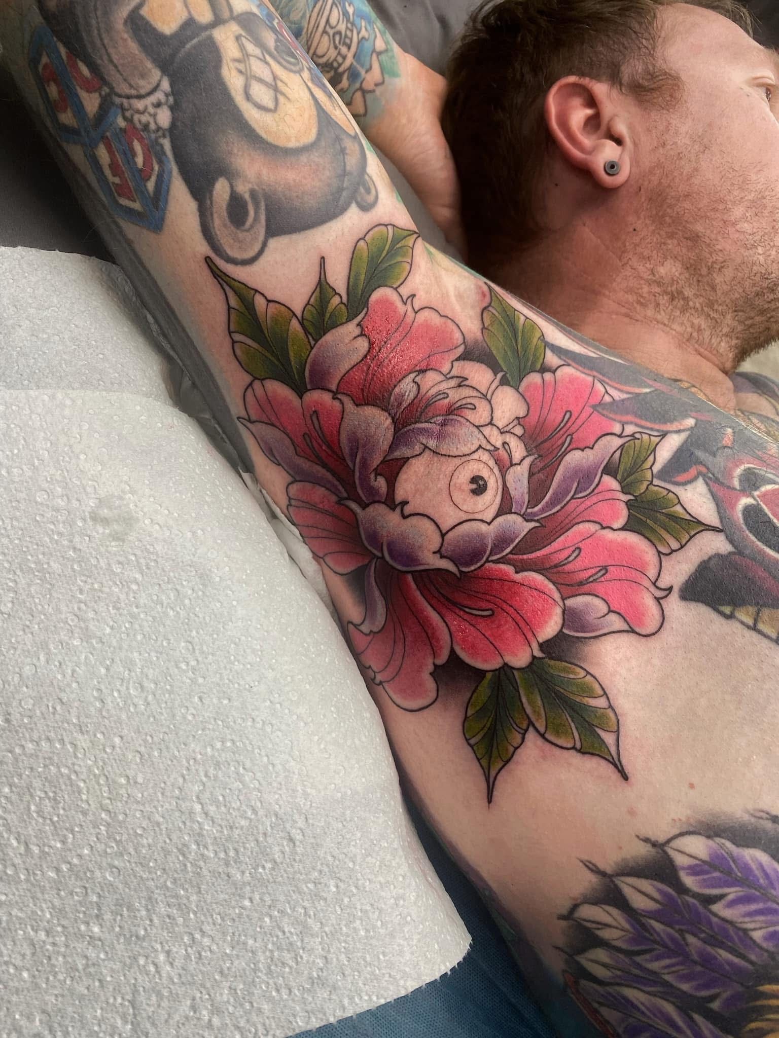 Tattoo of a vibrant pink and purple peony flower with green leaves on a person's arm. — Whitsunday Tattooing Airlie Beach in Whitsundays, QLD