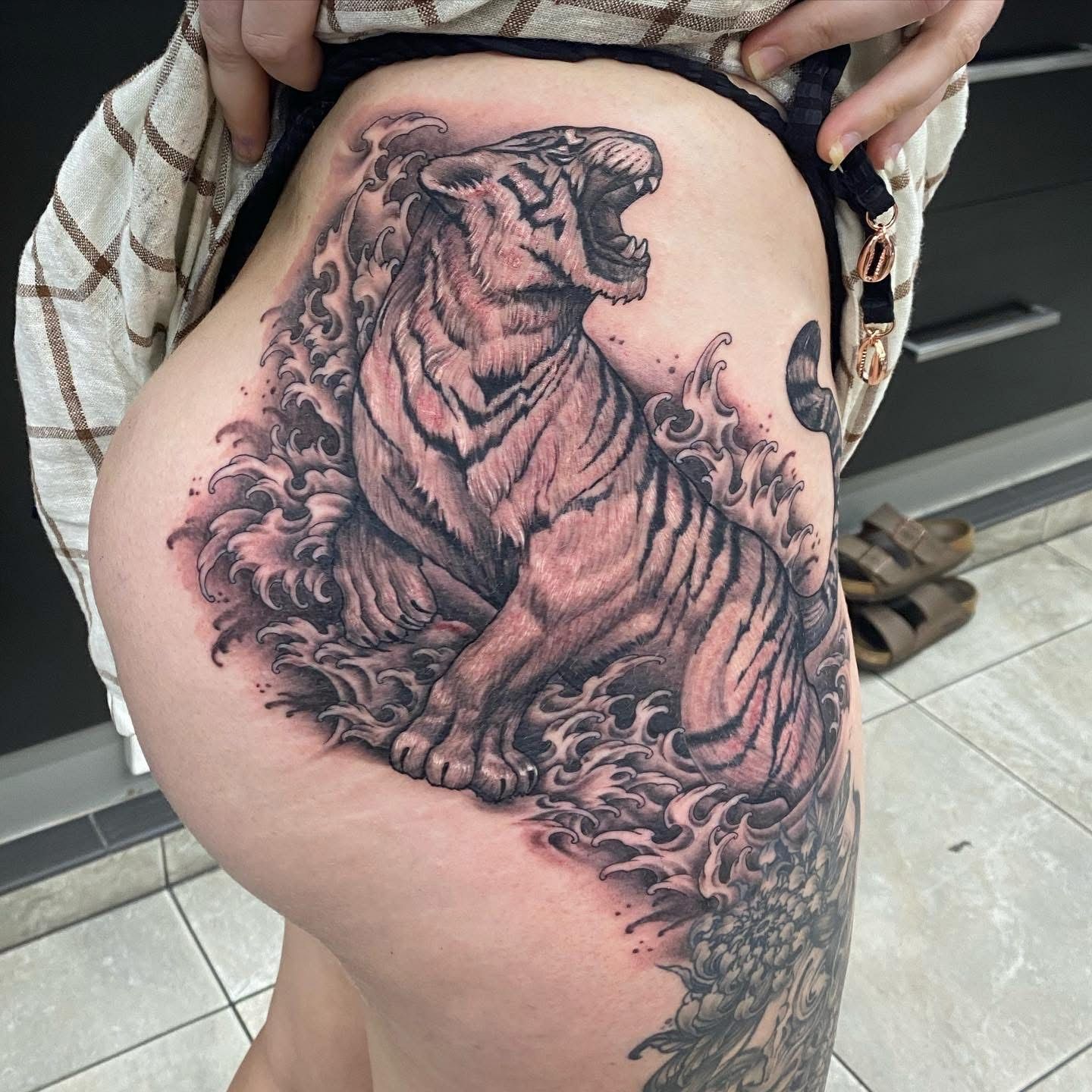 Tattoo of a roaring tiger surrounded by water swirls on a person's hip and thigh. — Whitsunday Tattooing Airlie Beach in Whitsundays, QLD