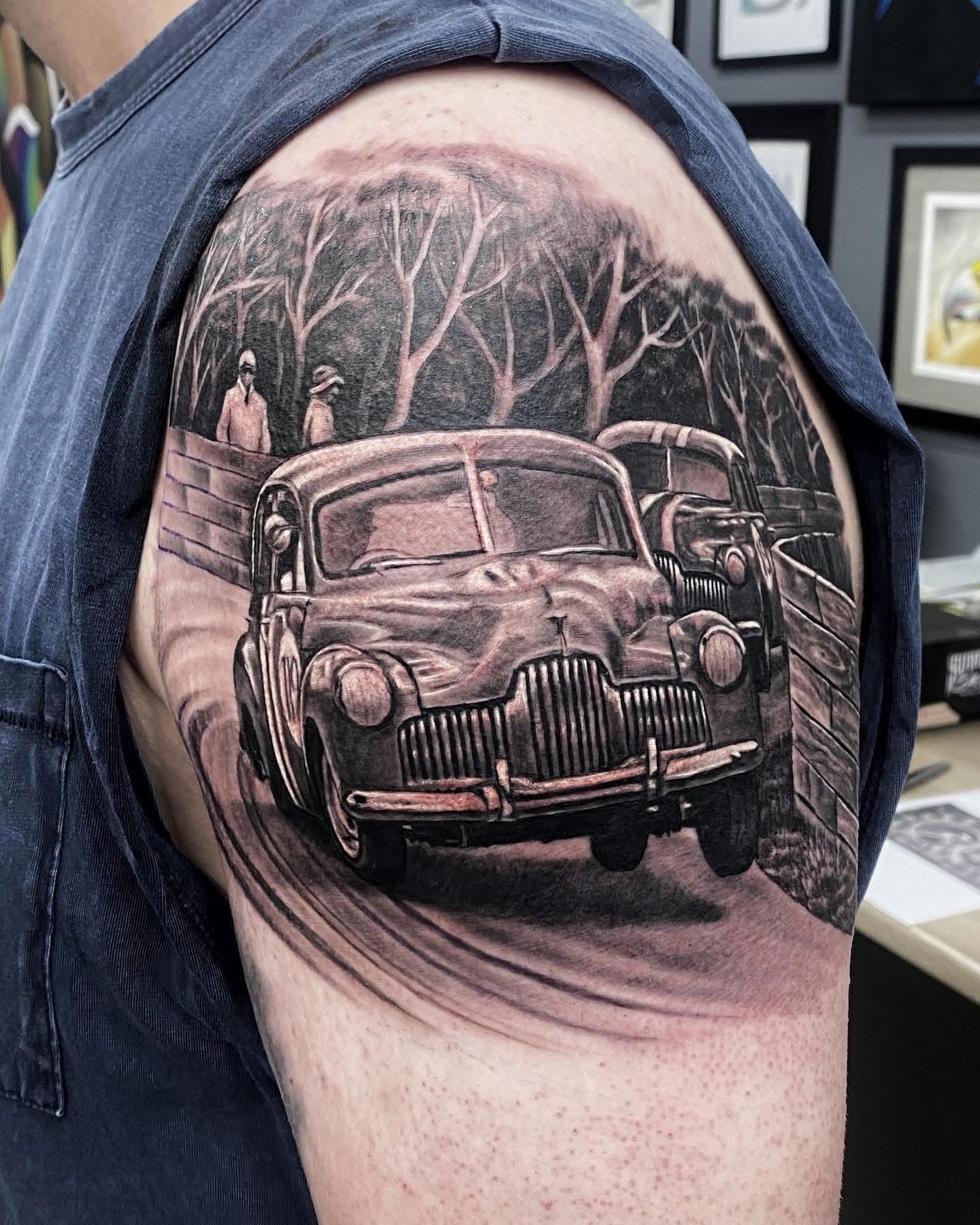 Black and gray tattoo of a vintage car driving on a road surrounded by trees and figures on an arm. — Whitsunday Tattooing Airlie Beach in Whitsundays, QLD