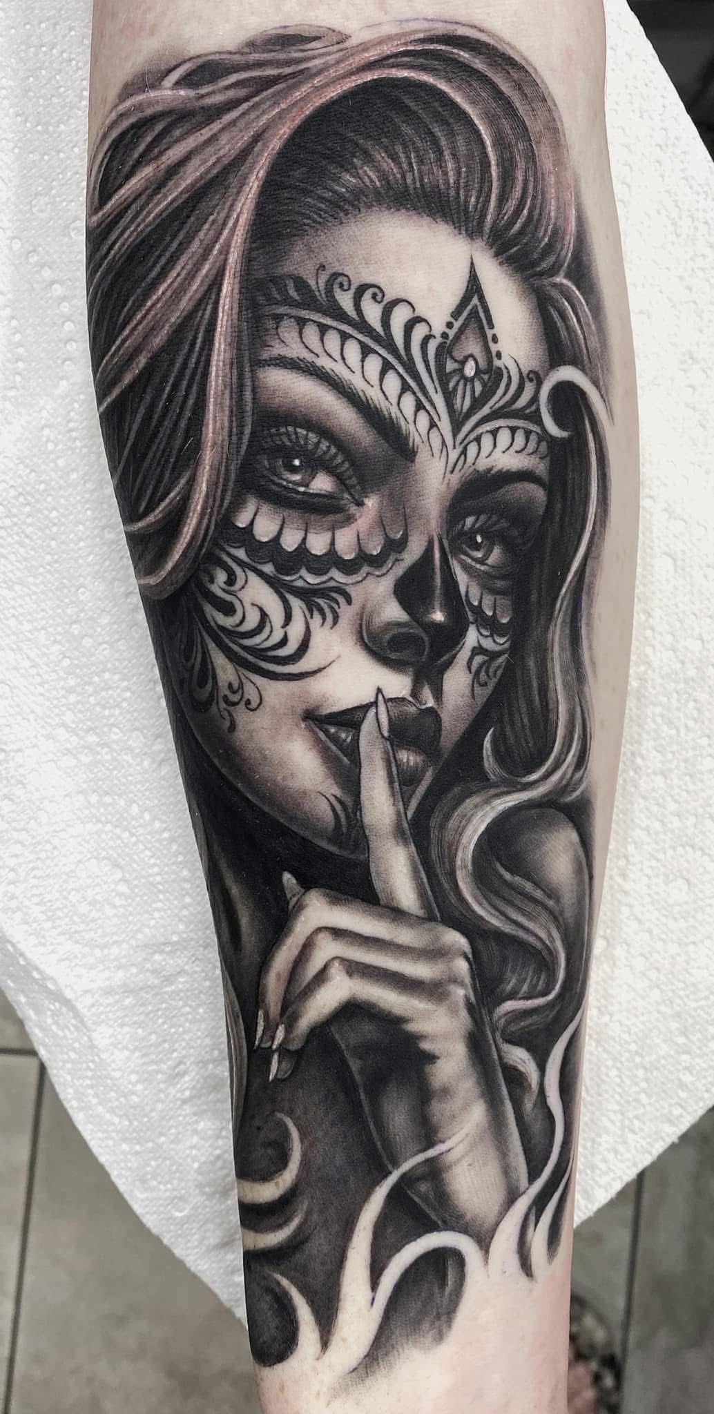 Tattoo of a woman with sugar skull makeup holding a finger to her lips, on a forearm. Black and white. — Whitsunday Tattooing Airlie Beach in Whitsundays, QLD