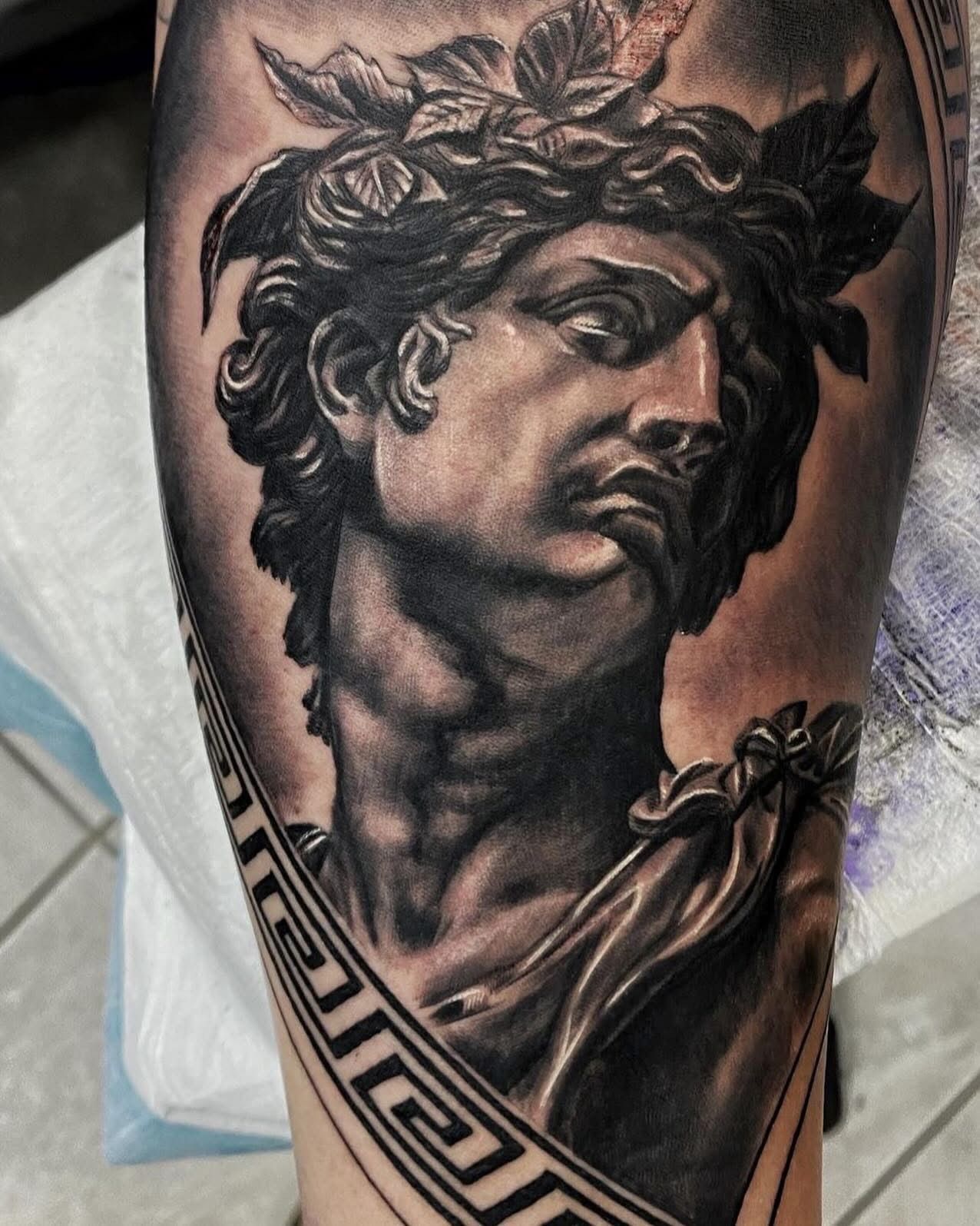 Black and gray tattoo of a classical bust with a laurel wreath on an arm. Greek key border. — Whitsunday Tattooing Airlie Beach in Whitsundays, QLD