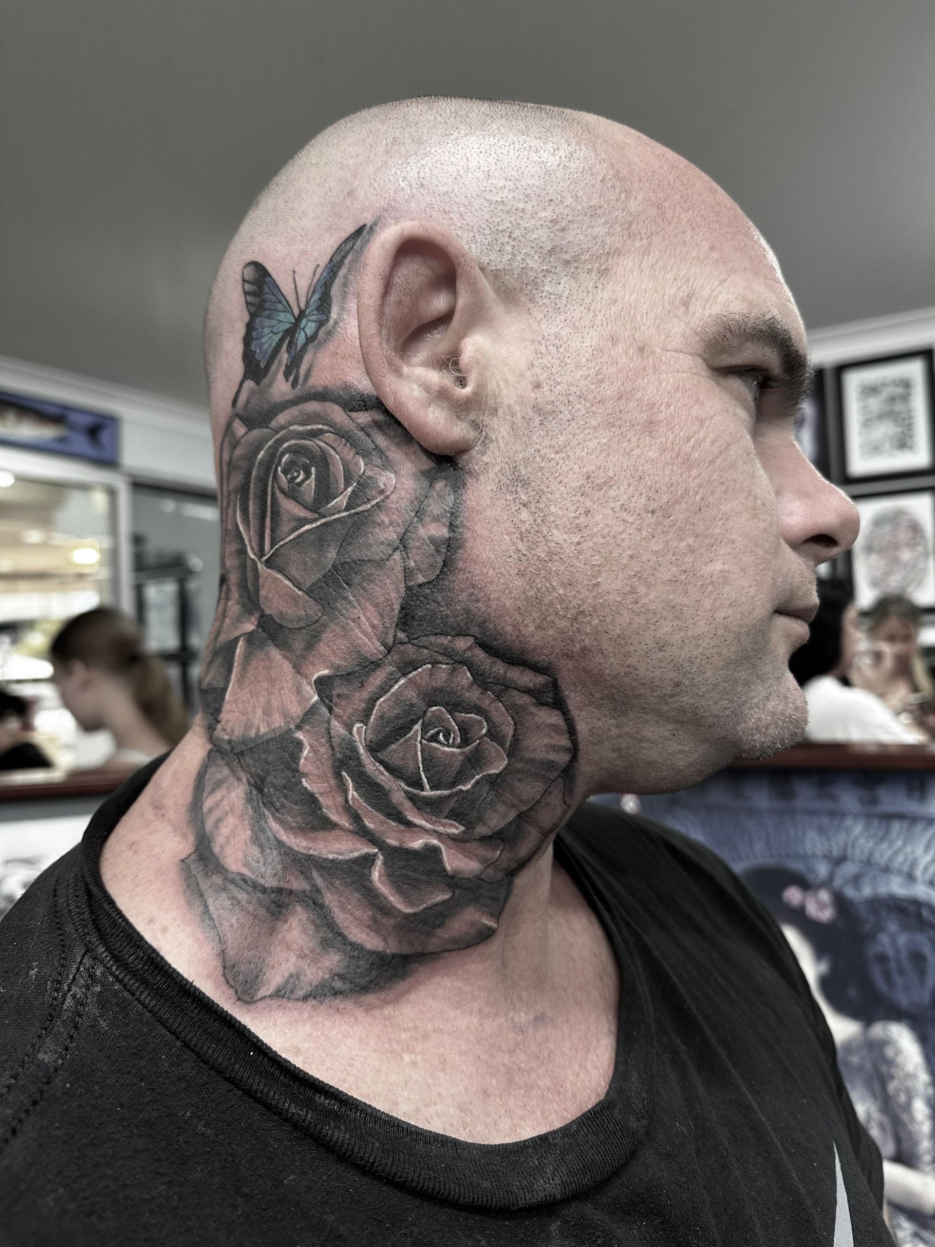 Man with a large, detailed rose tattoo on his neck and behind his ear; butterfly visible above. — Whitsunday Tattooing Airlie Beach in Whitsundays, QLD