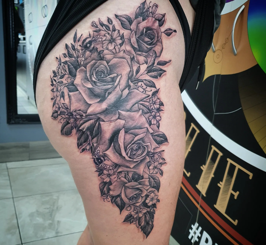 Black and gray roses tattoo on a person's upper thigh, with leaves and small flowers around them. — Whitsunday Tattooing Airlie Beach in Whitsundays, QLD