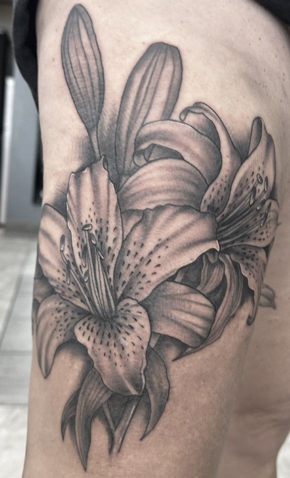 Black and grey lily tattoo on skin, featuring open blooms and buds. — Whitsunday Tattooing Airlie Beach in Whitsundays, QLD