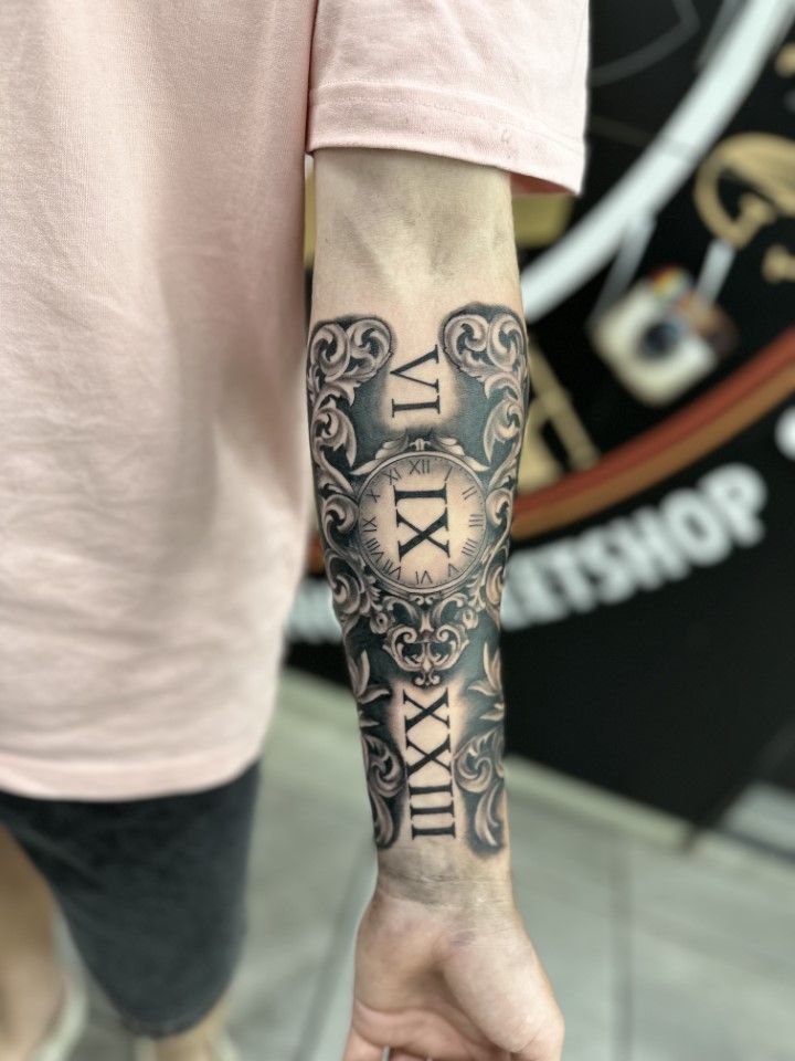 Arm tattoo: ornate black design with Roman numerals. — Whitsunday Tattooing Airlie Beach in Whitsundays, QLD