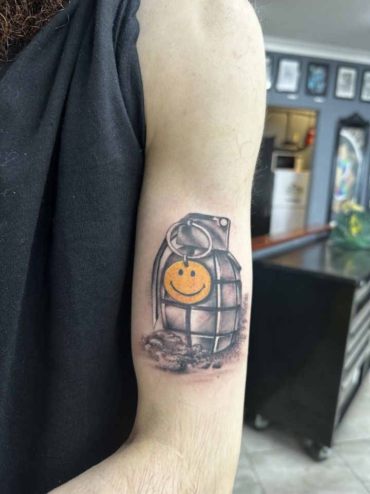 Tattoo of a grenade with a smiley face on a person's upper arm, in a tattoo parlor. — Whitsunday Tattooing Airlie Beach in Whitsundays, QLD