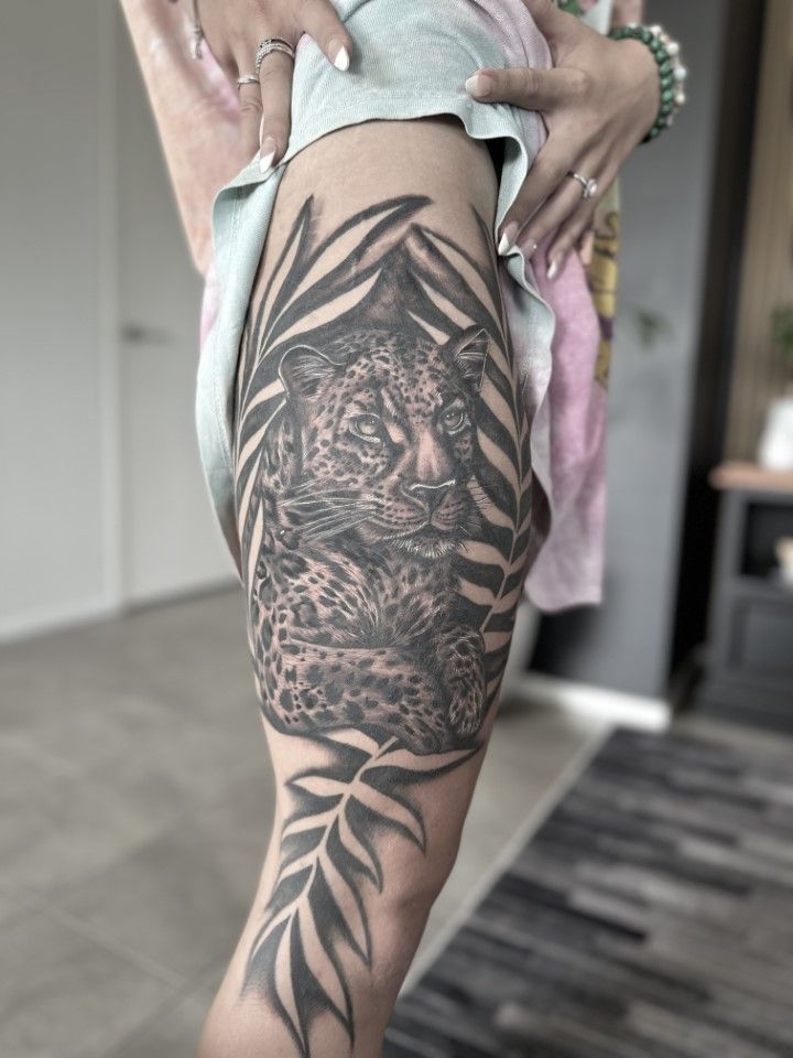 Black and gray leopard tattoo on a leg, surrounded by leafy foliage. — Whitsunday Tattooing Airlie Beach in Whitsundays, QLD