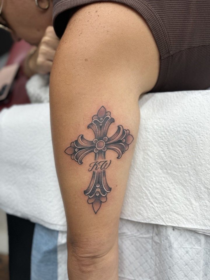 Tattoo of a decorative cross with initials on an arm. Silver and black. — Whitsunday Tattooing Airlie Beach in Whitsundays, QLD