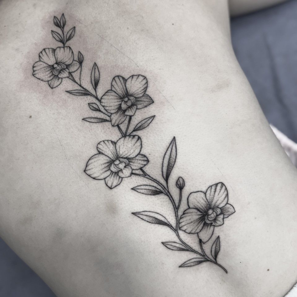 Black ink floral vine tattoo on a person's back. Four flowers with leaves.
