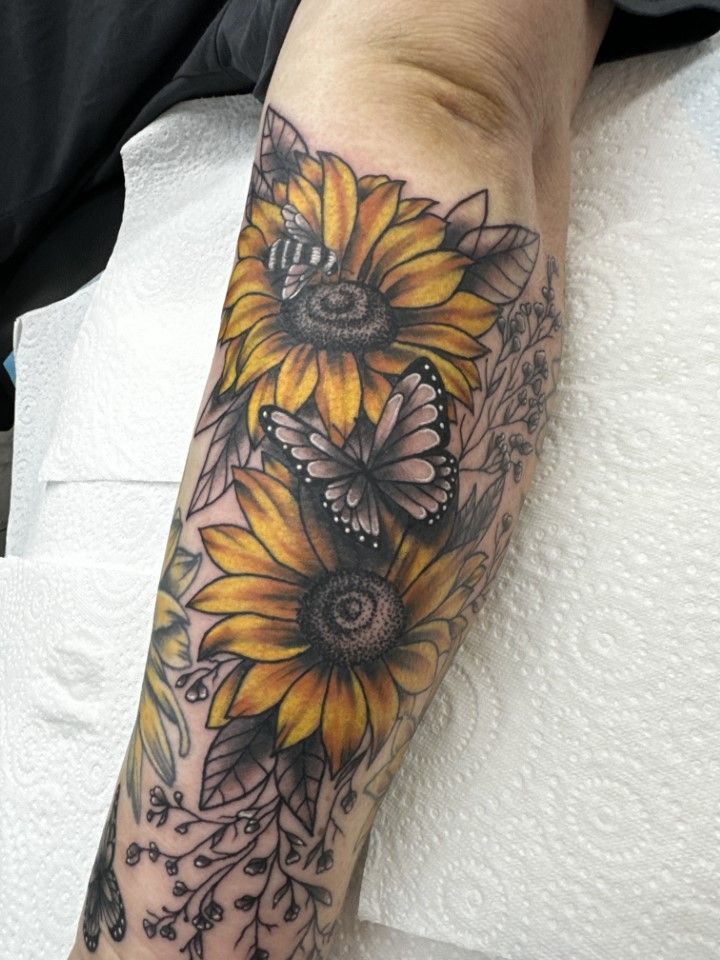 Tattoo of two yellow sunflowers and a butterfly on an arm. Dark leaves and gray details. — Whitsunday Tattooing Airlie Beach in Whitsundays, QLD