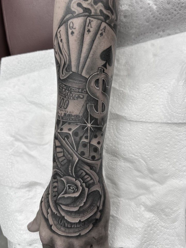 Black and gray arm tattoo: playing cards, dollar sign, dice, a rose, and smoke. — Whitsunday Tattooing Airlie Beach in Whitsundays, QLD