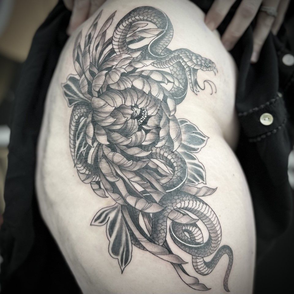 Tattoo of a snake coiled around a flower on a person's thigh, in black ink. — Whitsunday Tattooing Airlie Beach in Whitsundays, QLD