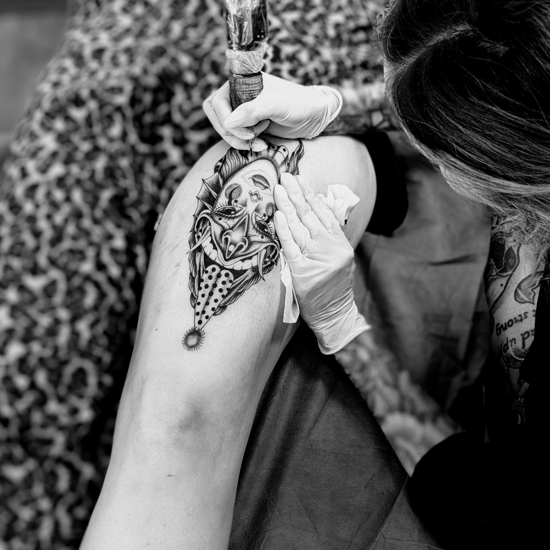 Tattoo artist in gloves working on a detailed black and white design on a person's leg.