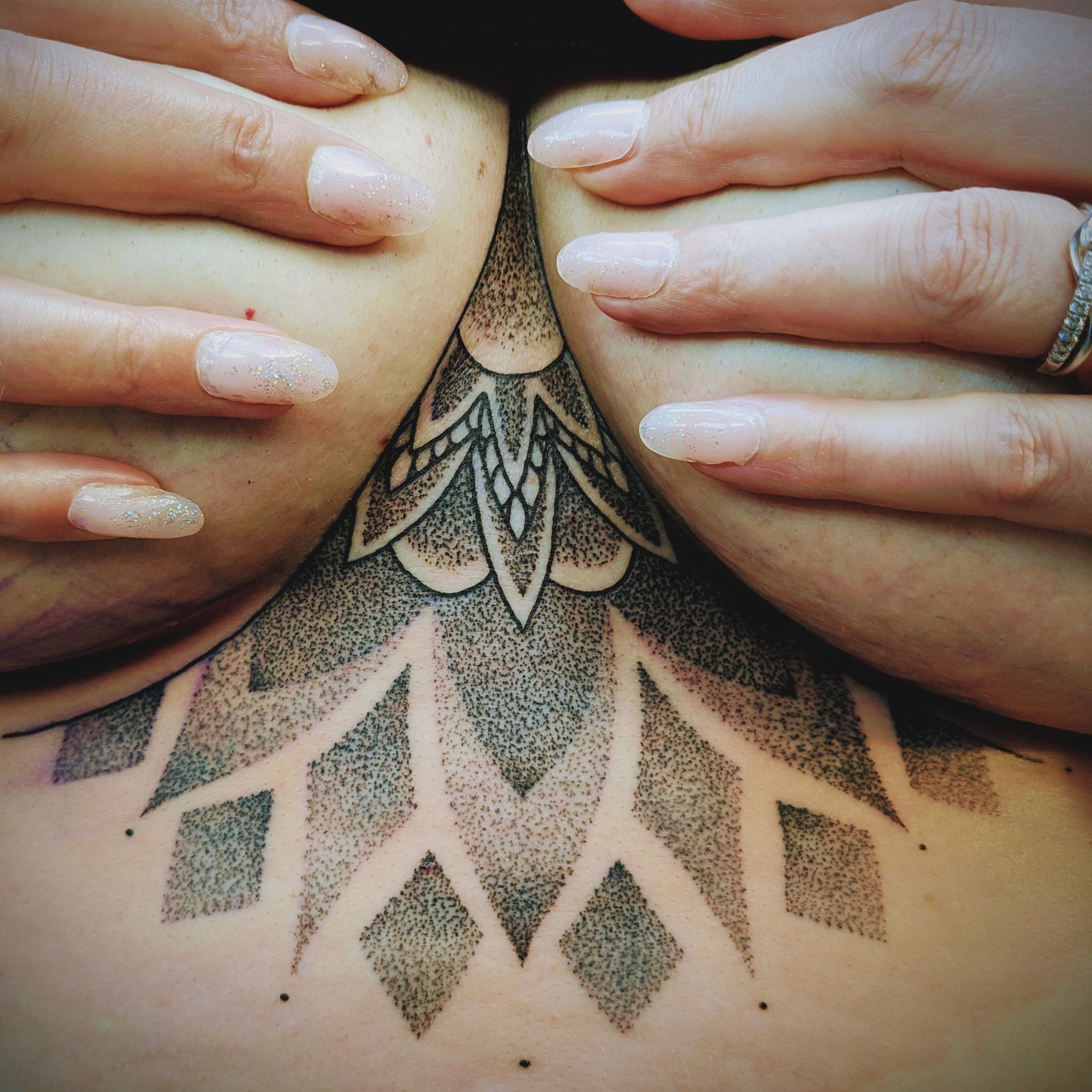 Hands holding breasts, revealing a black geometric chest tattoo.