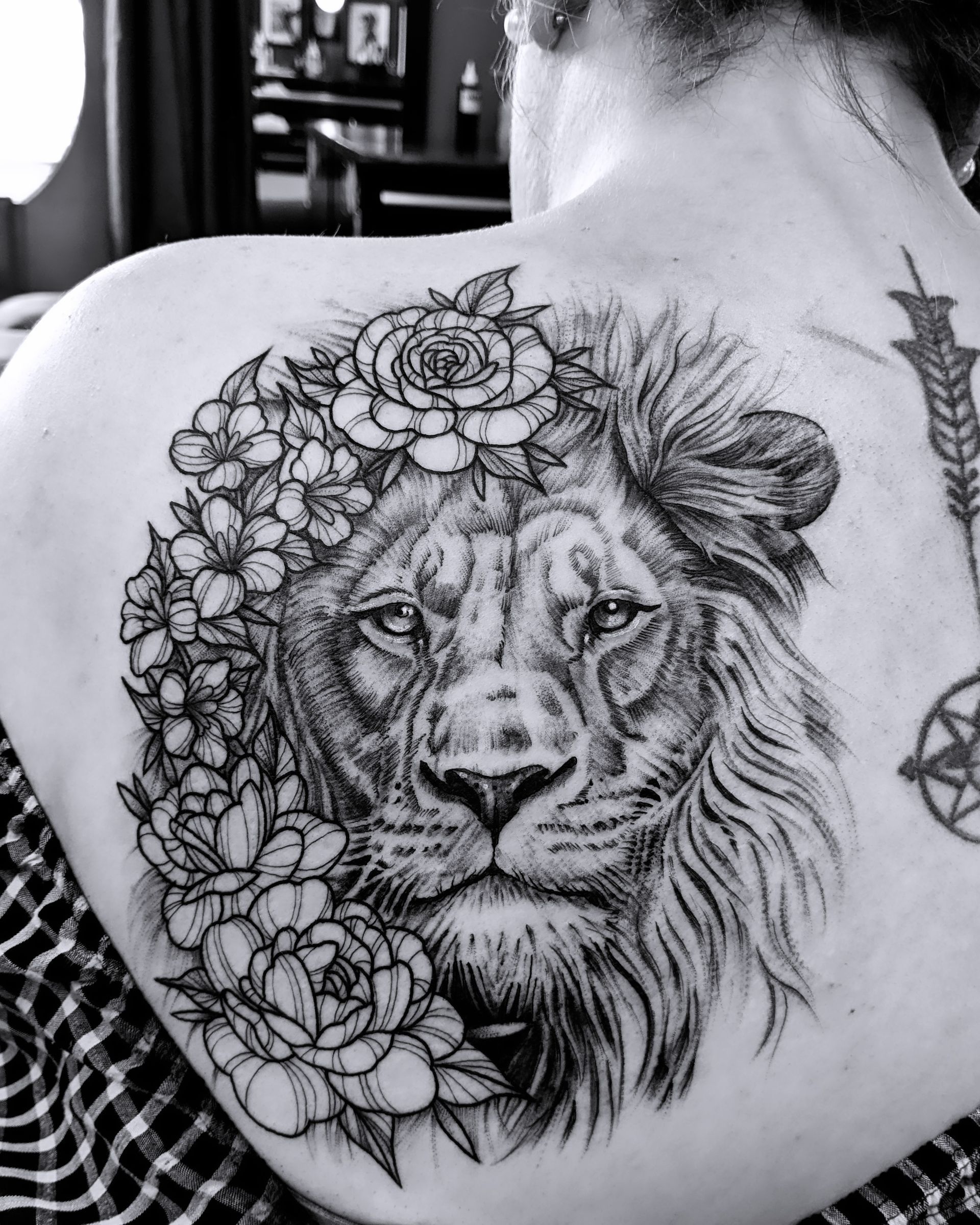 Black and white tattoo of a lion's head wearing a floral crown on a person's back.