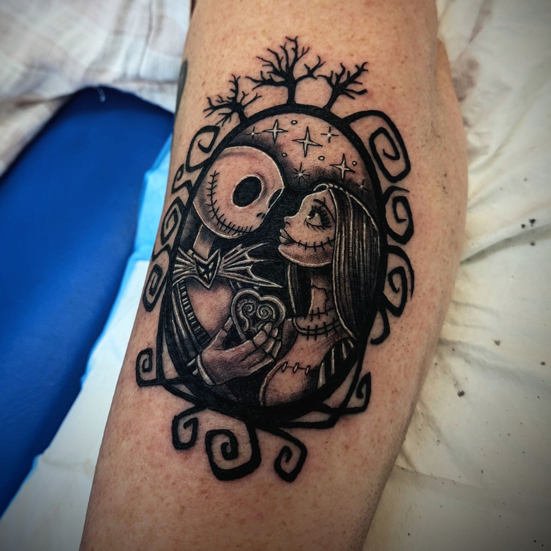 Tattoo of Jack and Sally from The Nightmare Before Christmas, framed in a dark oval with swirling details.