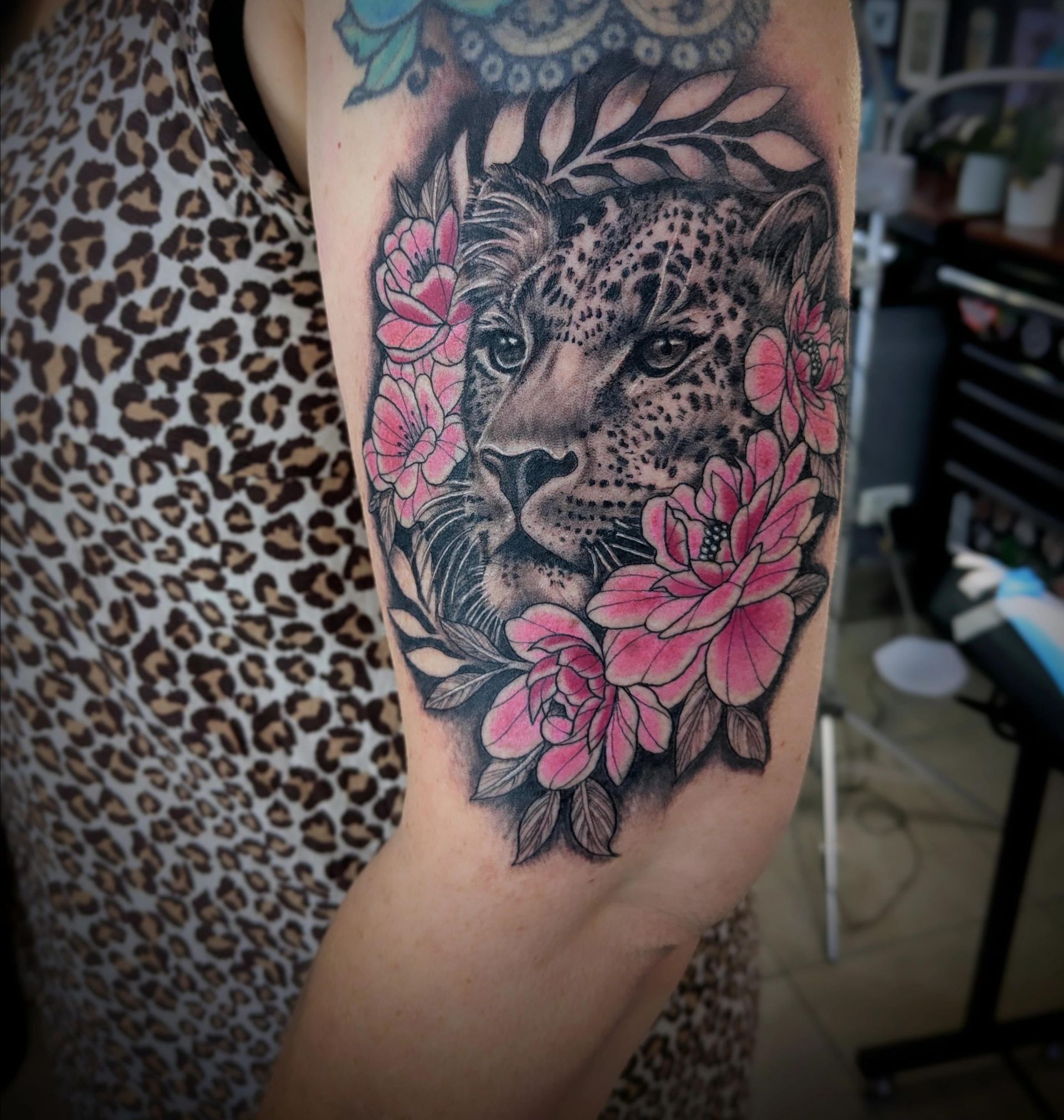 Tattoo of a leopard's face surrounded by pink peonies and green leaves on an arm.