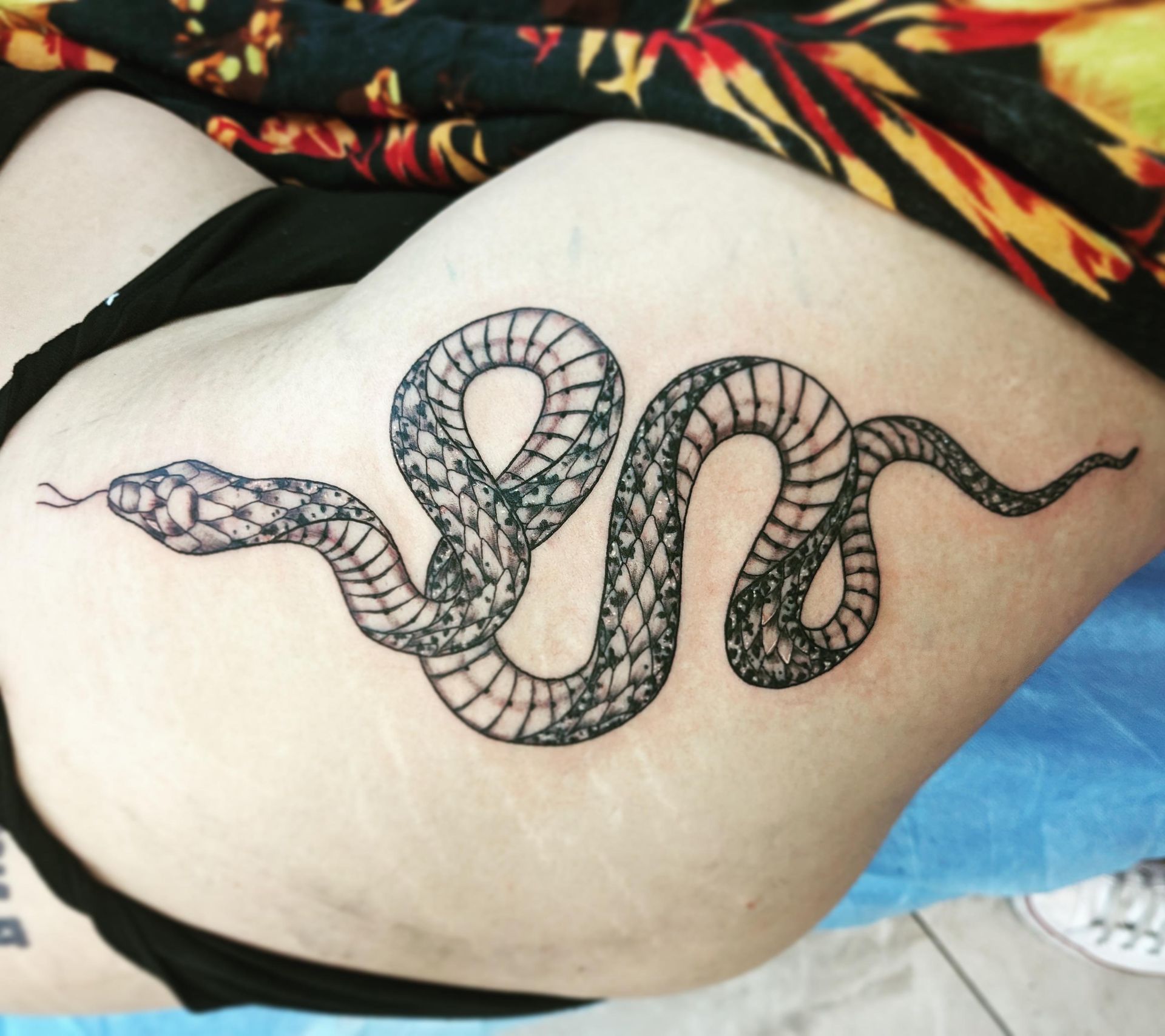 Black snake tattoo on a person's side, with scale details.
