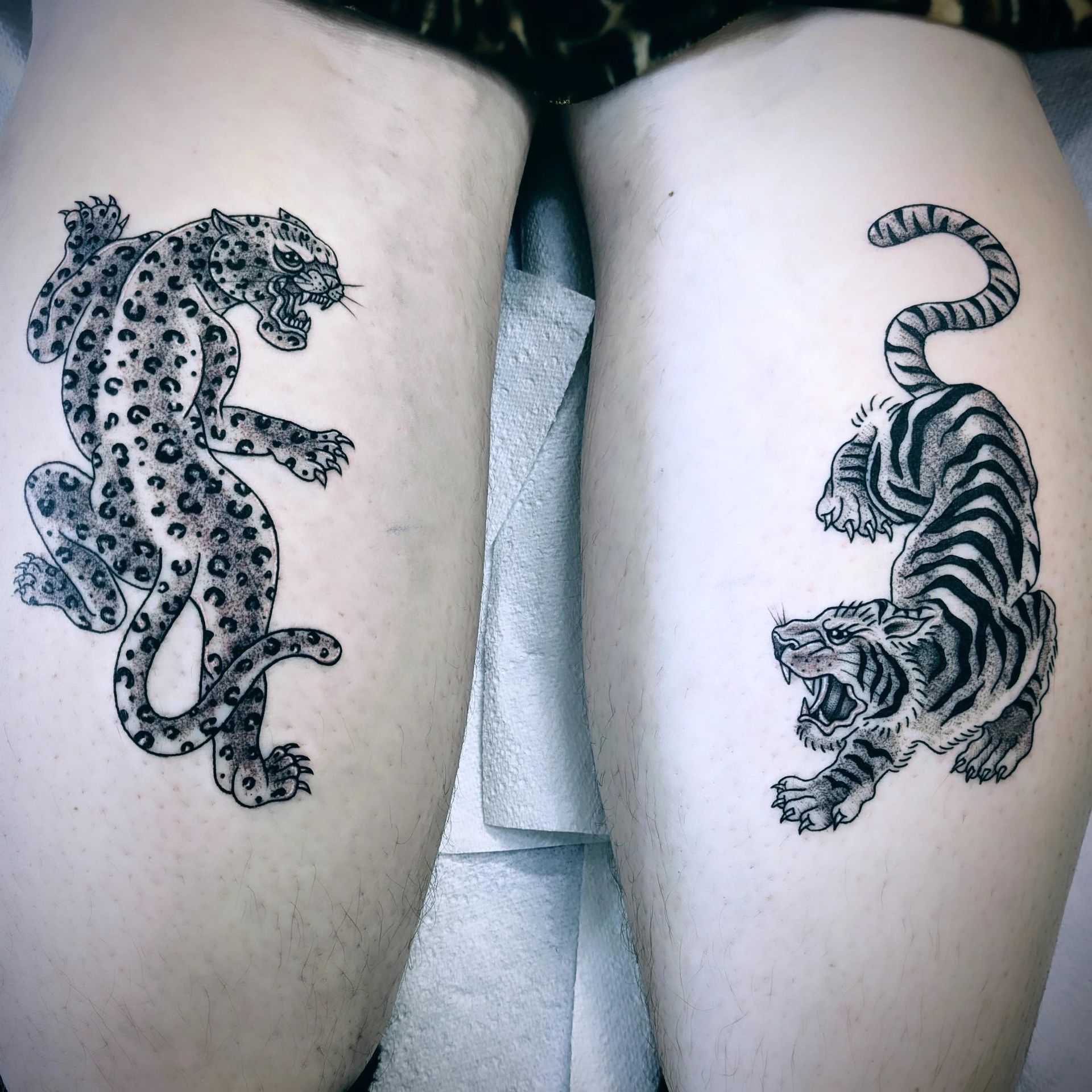 Two thigh tattoos: a snarling leopard and a striped tiger, both in black ink.