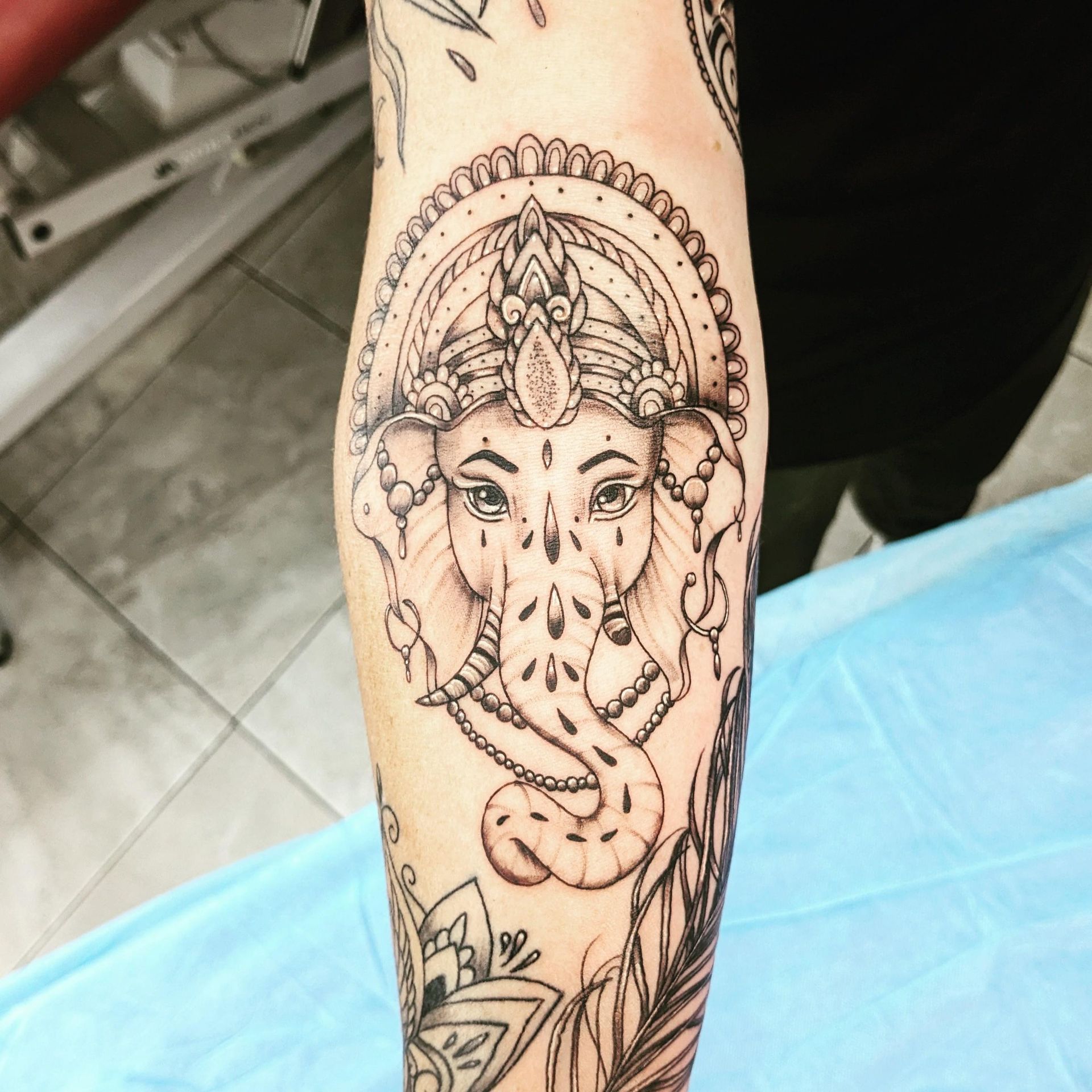 Black and white tattoo of Ganesha on an arm, with a detailed headdress and trunk.