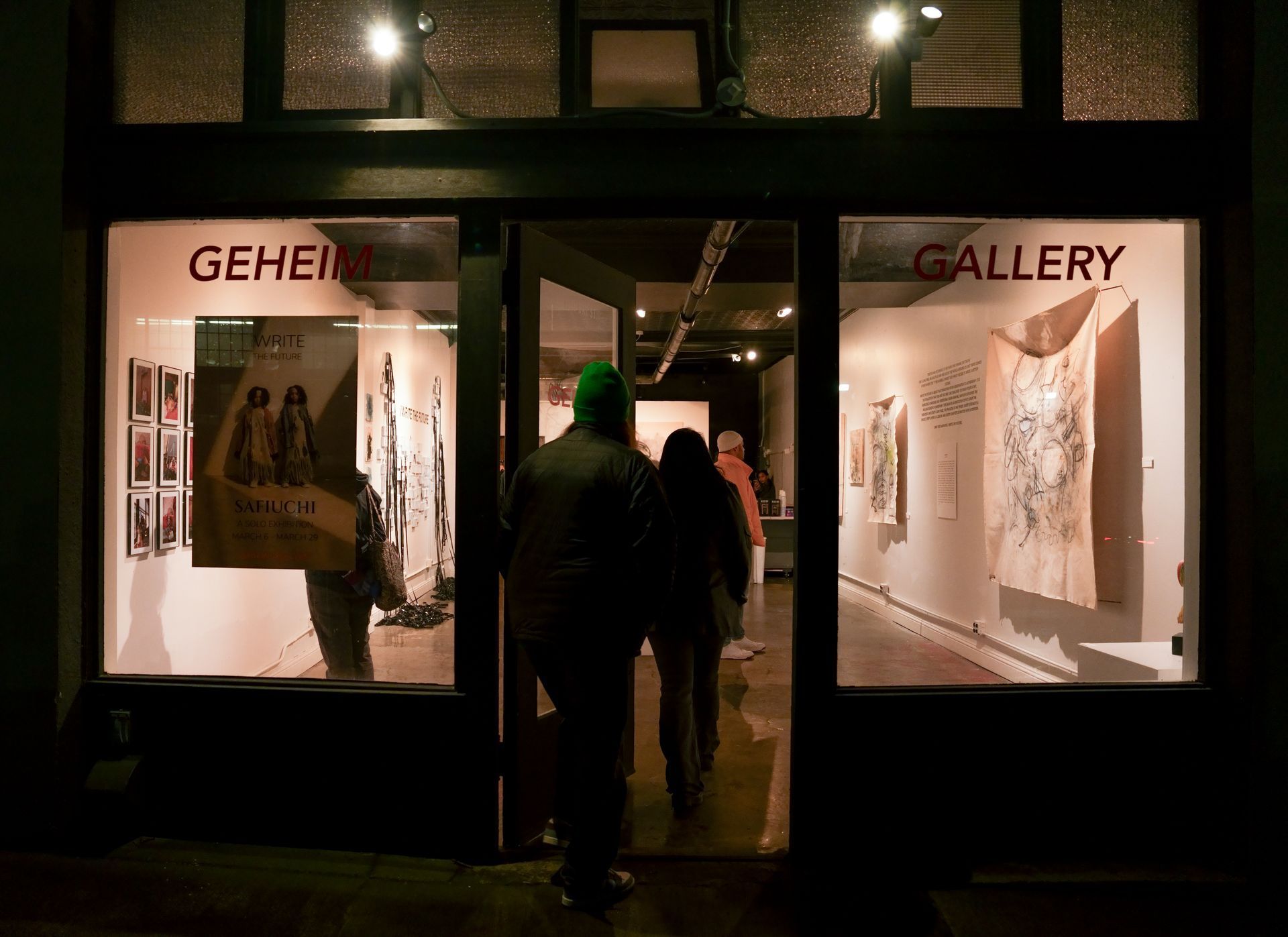 Two people walk through the open door of an art gallery titled 