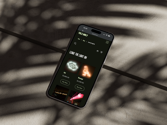 A smartphone displaying a music app interface with a dark theme, resting on a textured surface with palm leaf shadows.