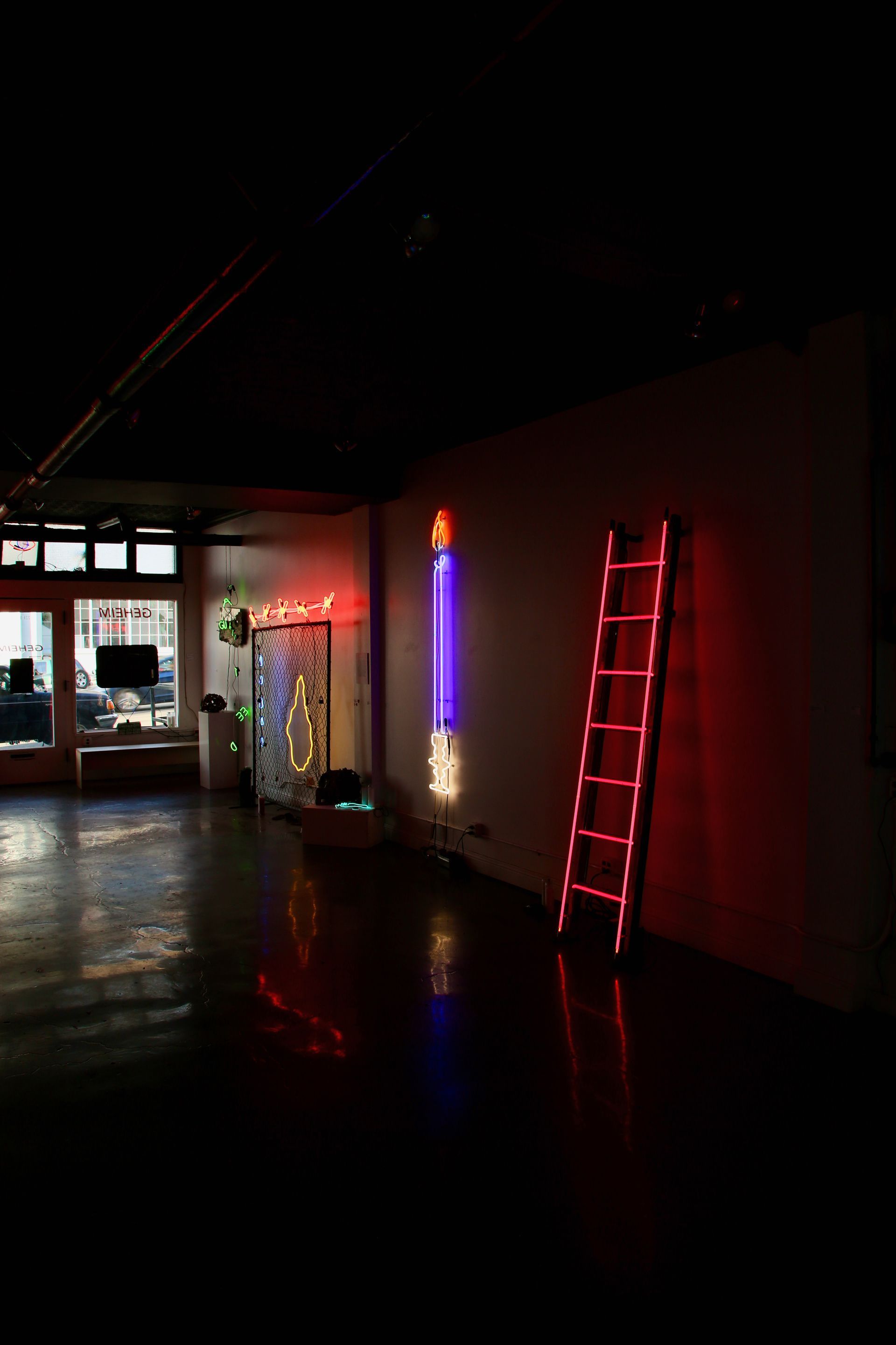 Pink wall with jeans hanging from a fluorescent light, by Yale Wolf. The jeans have dark stains.