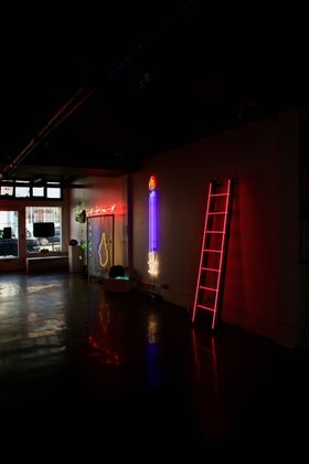 Yale Wolf - Geheim Gallery Pink wall with jeans hanging from a fluorescent light, by Yale Wolf. The jeans have dark stains.