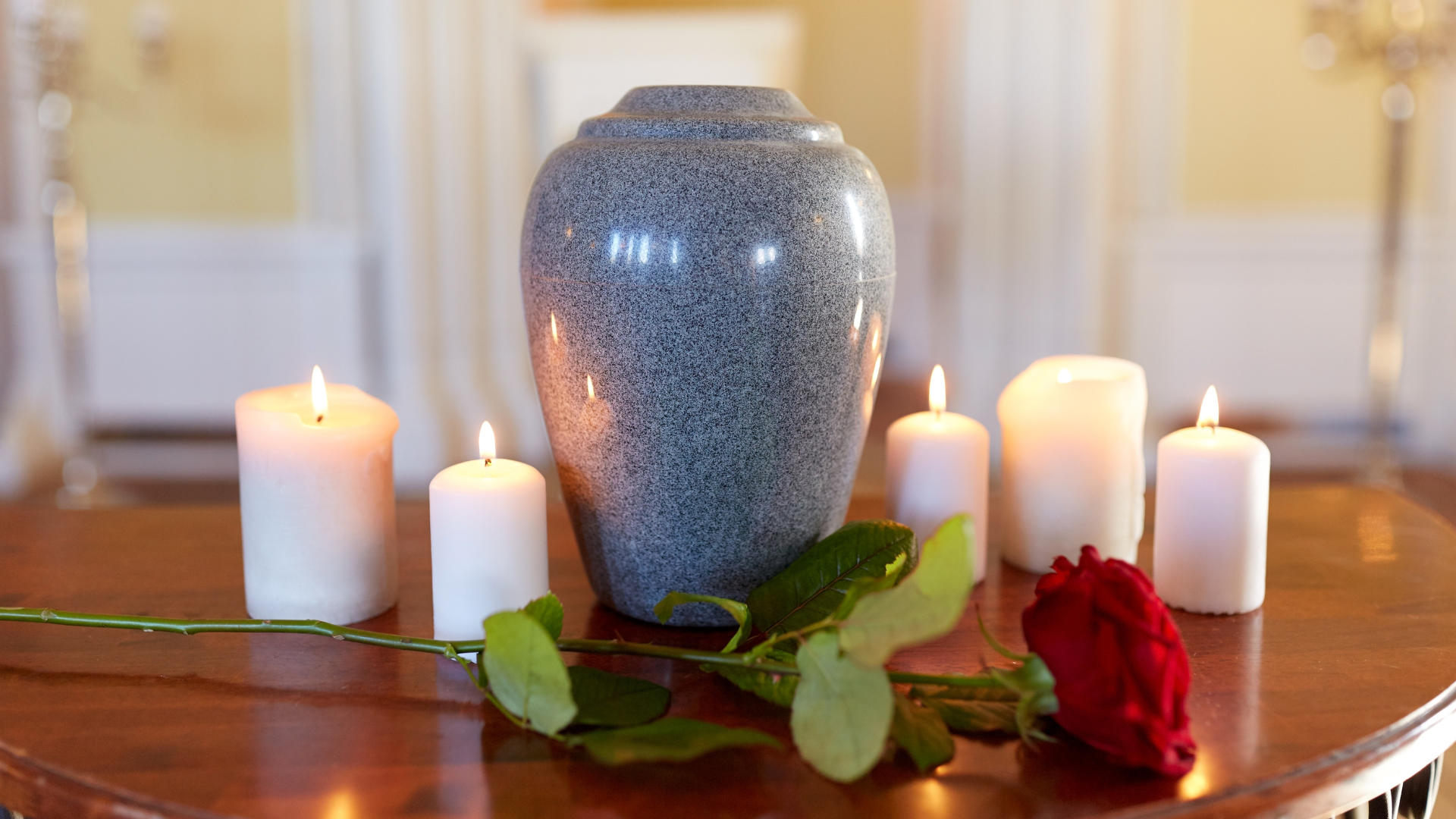 A vase with a rose and candles on a table.