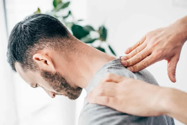 Man receiving neck and shoulder massage in a brightly lit room.