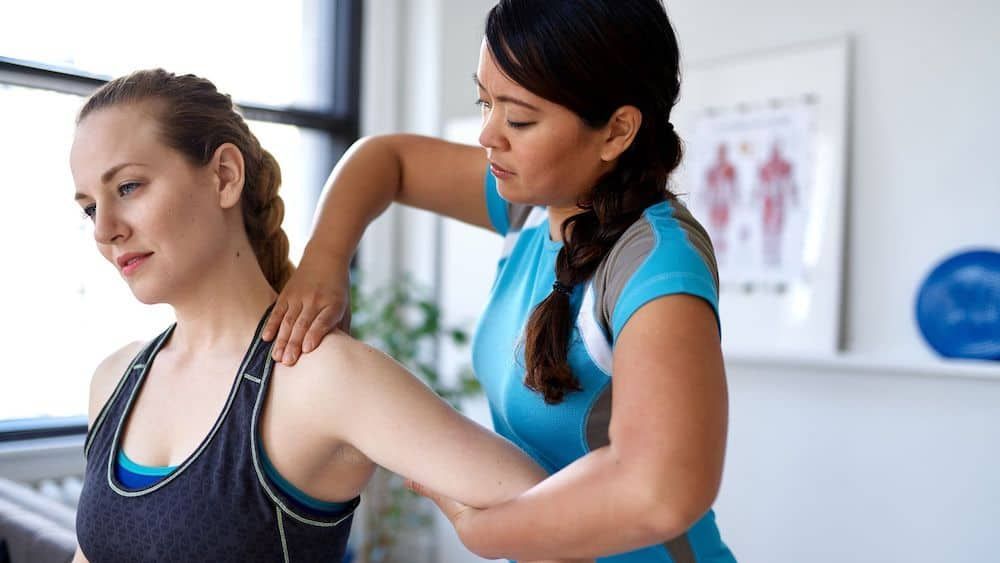 A woman in athletic wear receives physical therapy from a therapist in a bright office setting.