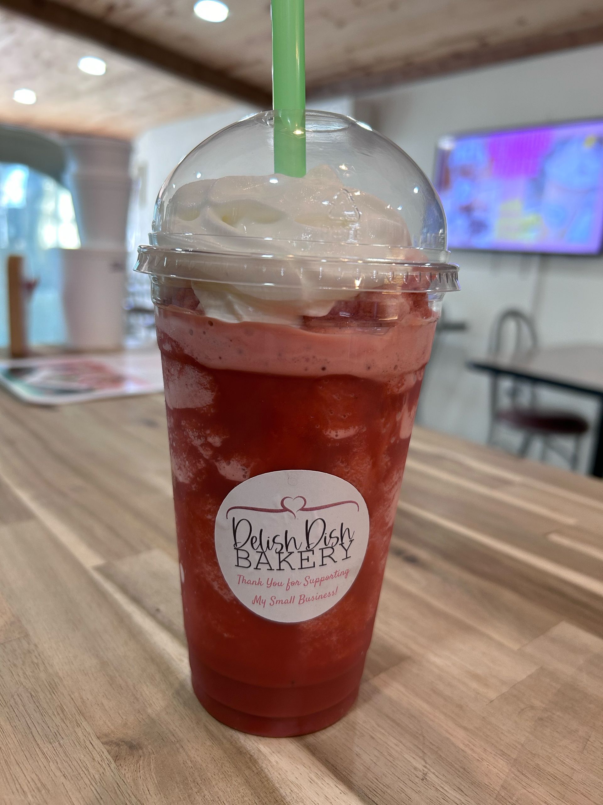 A cup of strawberry smoothie with whipped cream and a straw on a wooden table.