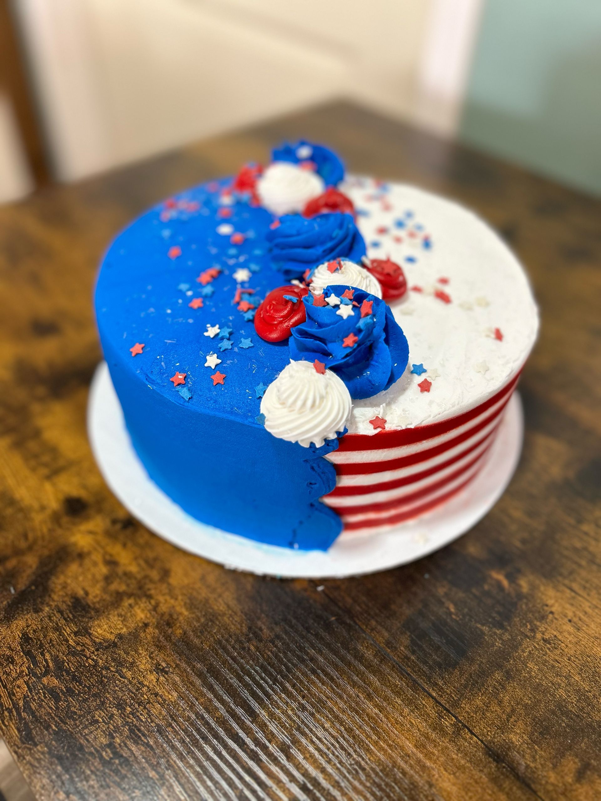 A red , white and blue cake is sitting on a wooden table.