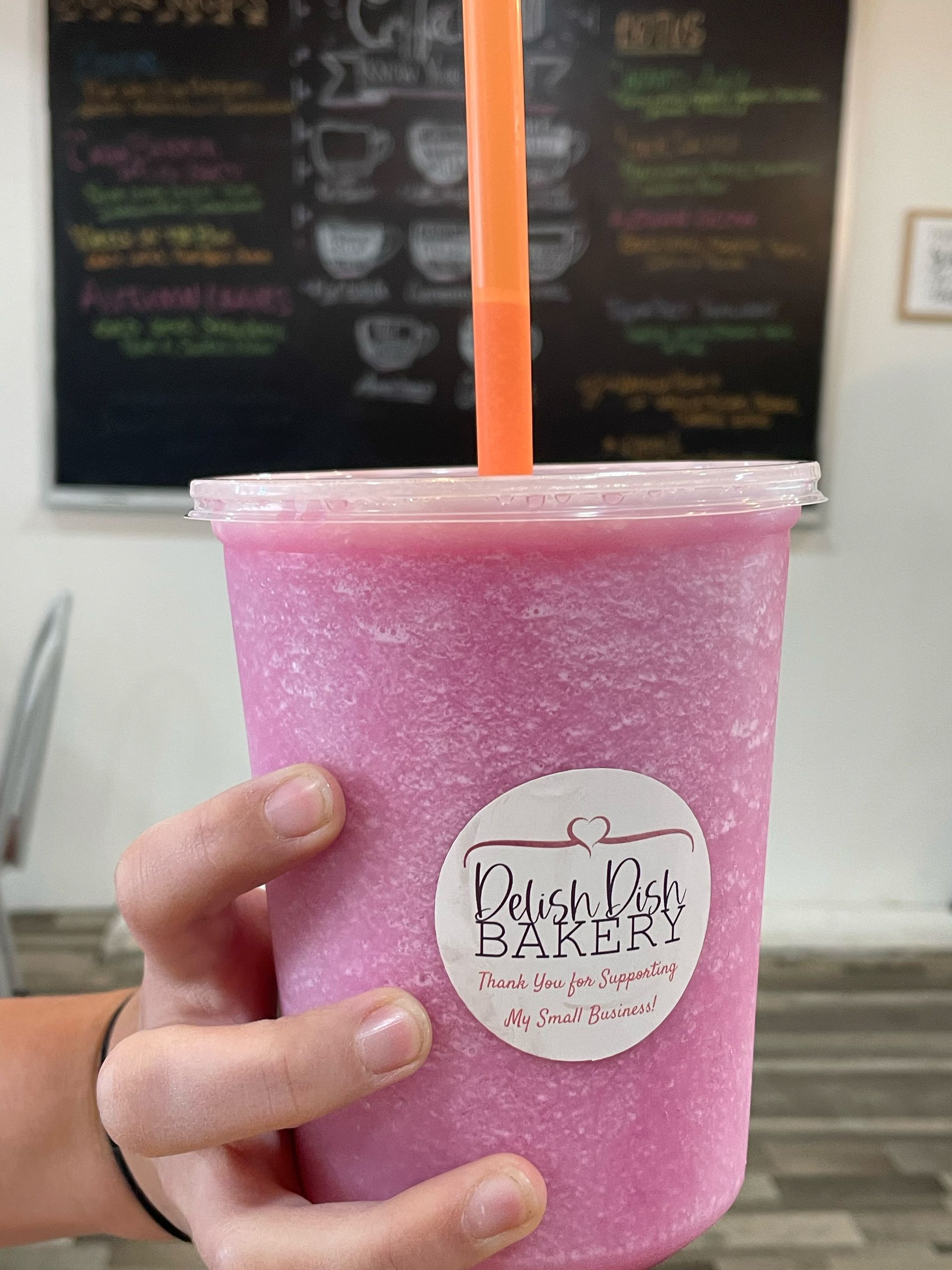 A person is holding a pink smoothie with an orange straw.