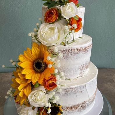 A three tiered wedding cake decorated with sunflowers and roses on a table.