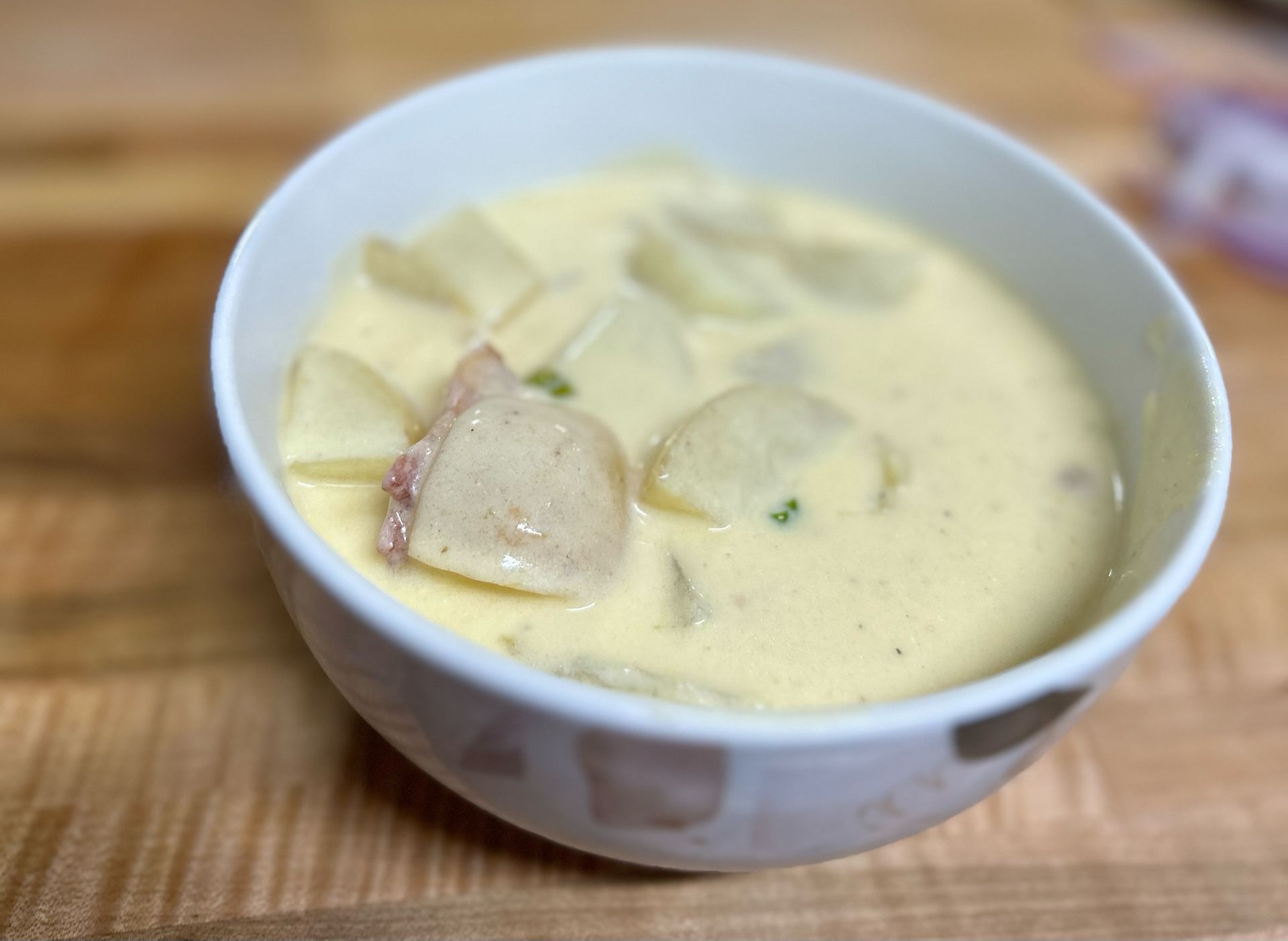 A bowl of soup with potatoes and cheese on a wooden table.