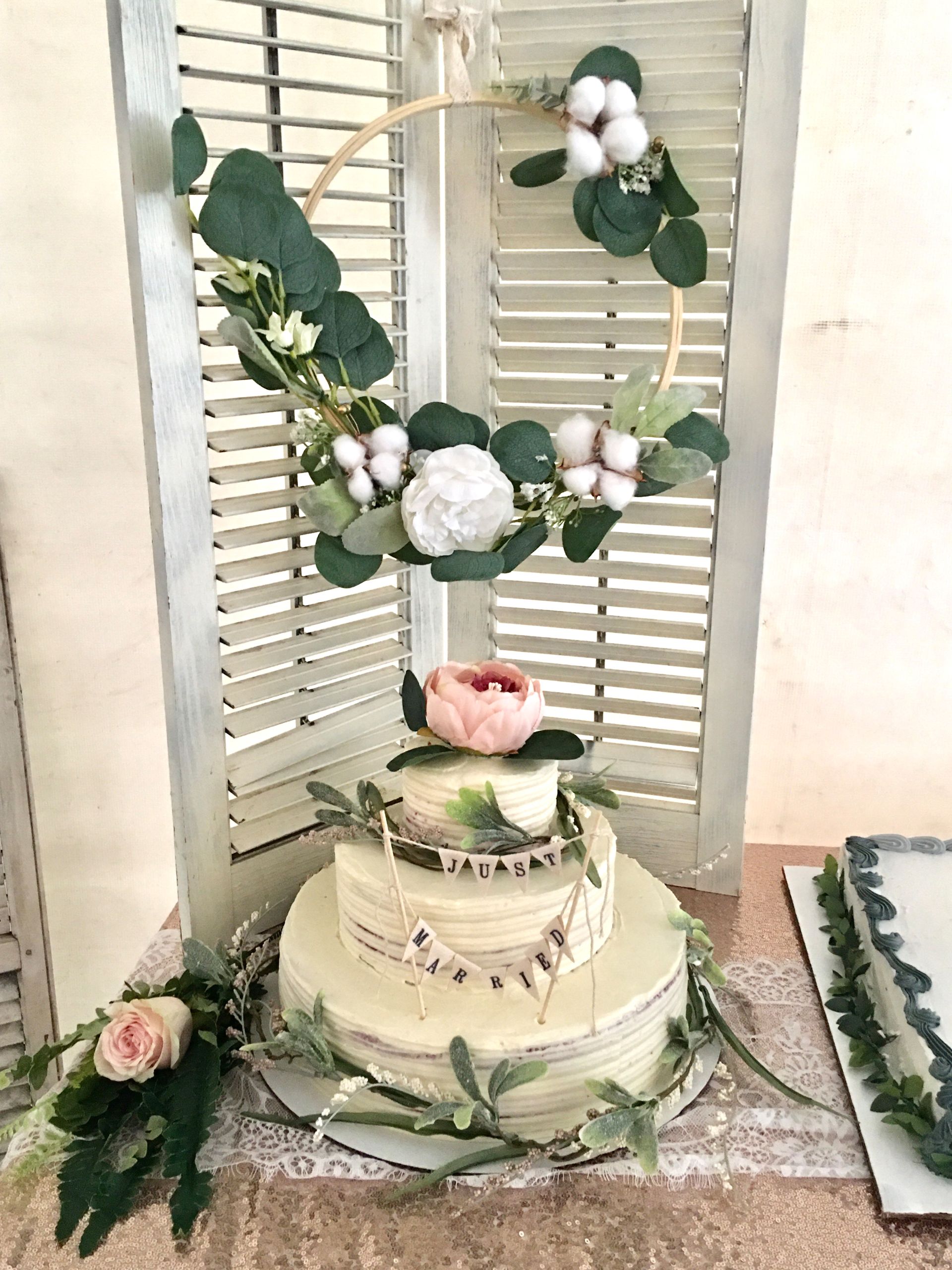 A wedding cake is sitting on top of a table next to a window shutter.