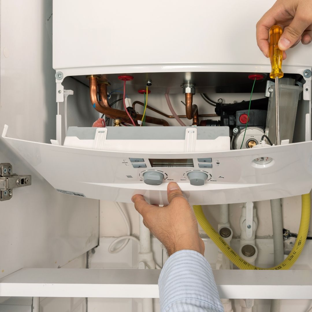 A man is sitting on the floor fixing an air conditioner.