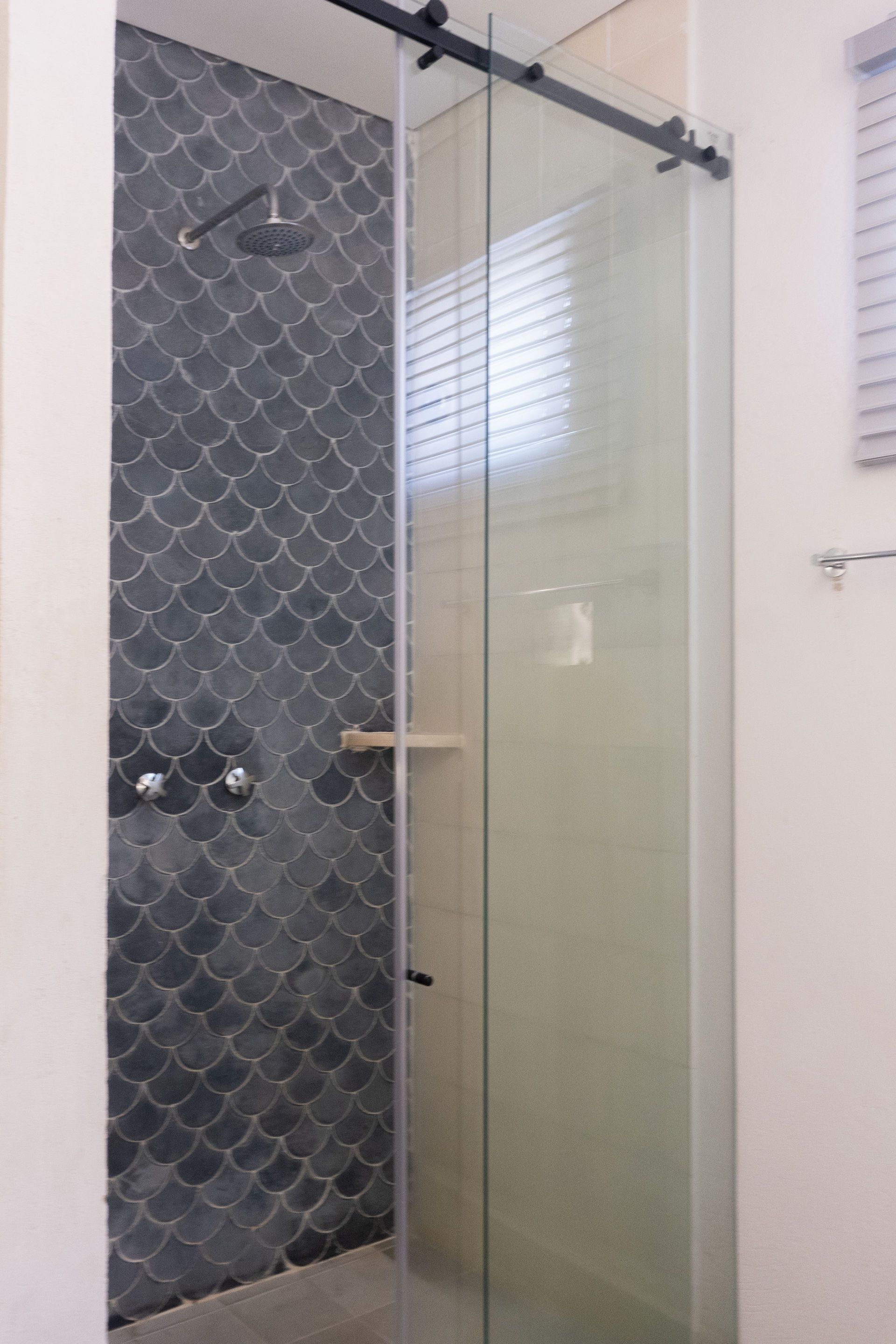 Ducha con pared de azulejos en escamas de pescado de color azul oscuro y puerta corrediza de vidrio transparente.