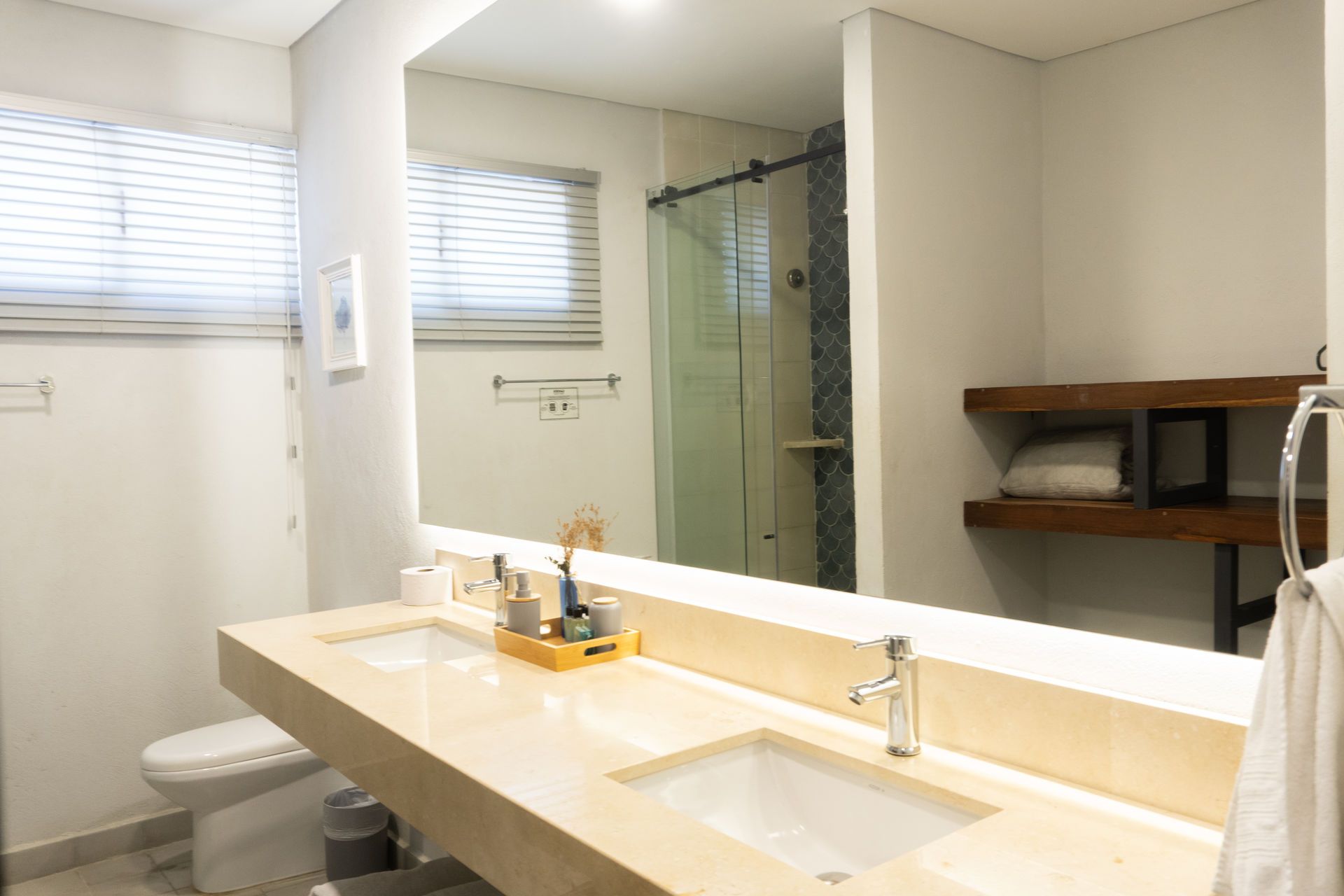 Baño moderno con dos lavabos, espejo grande y puerta de ducha de cristal.