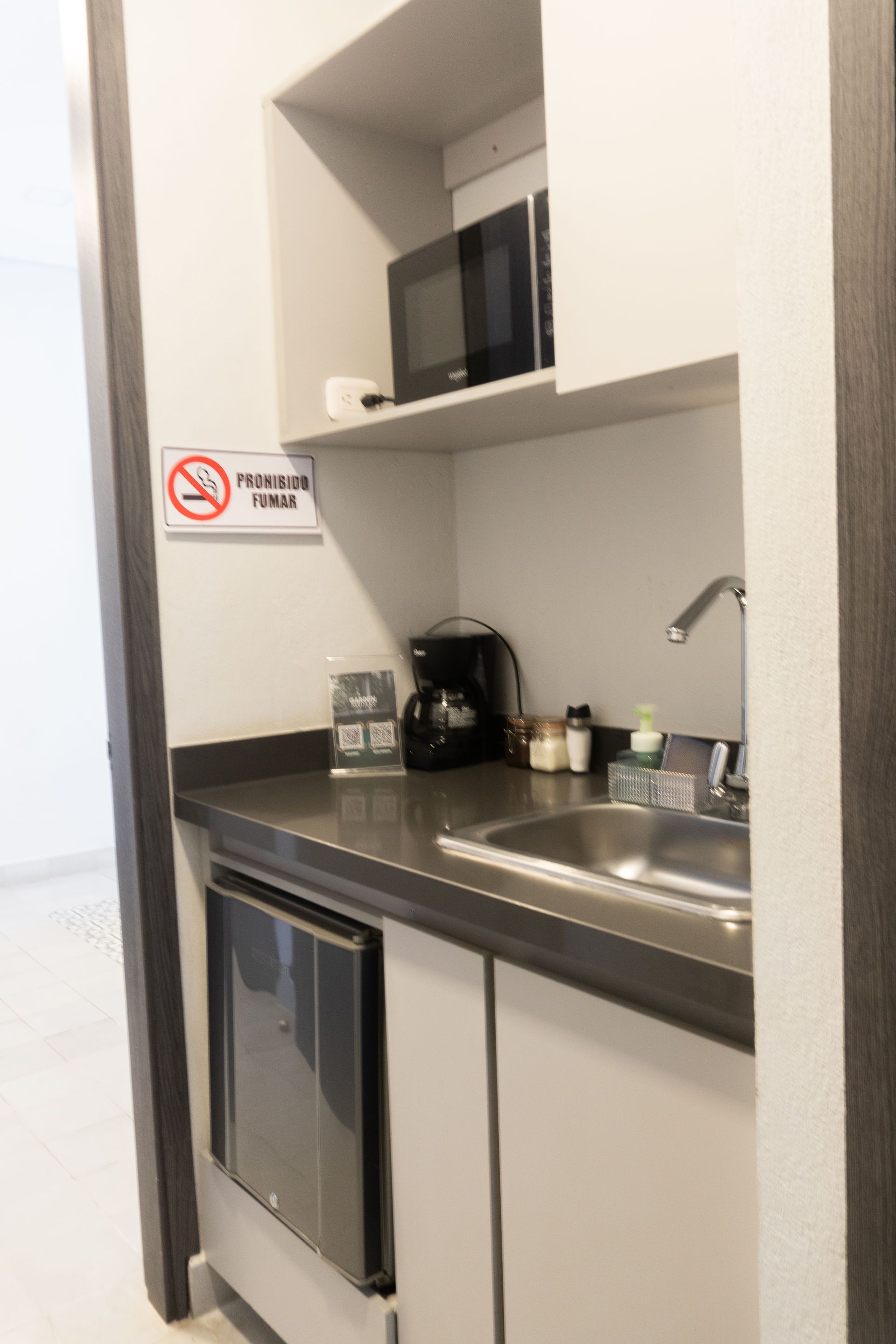 Pequeña cocina con microondas, cafetera, fregadero y mininevera.