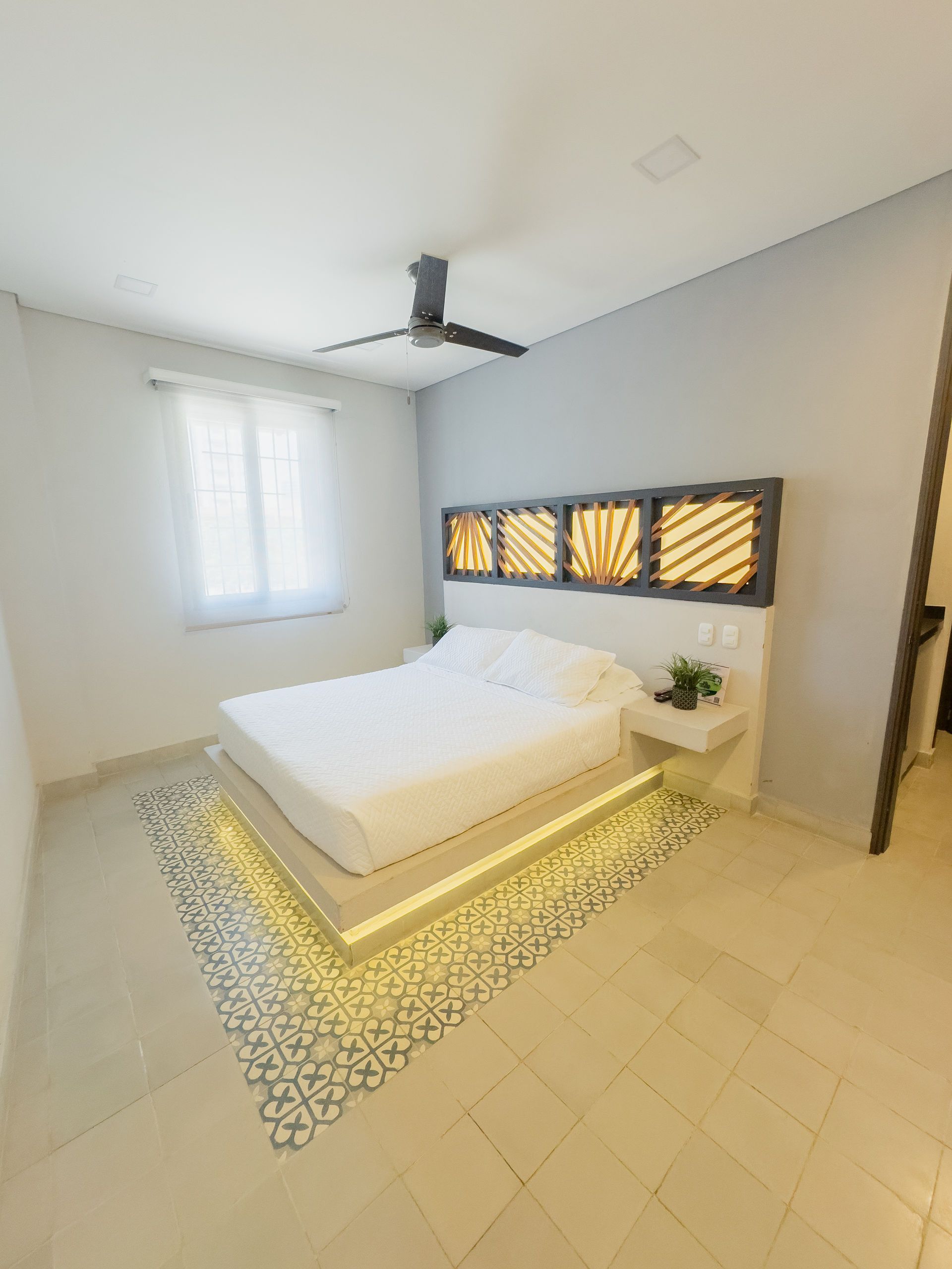 Dormitorio con estructura de cama moderna, cabecero decorativo e iluminación ambiental.