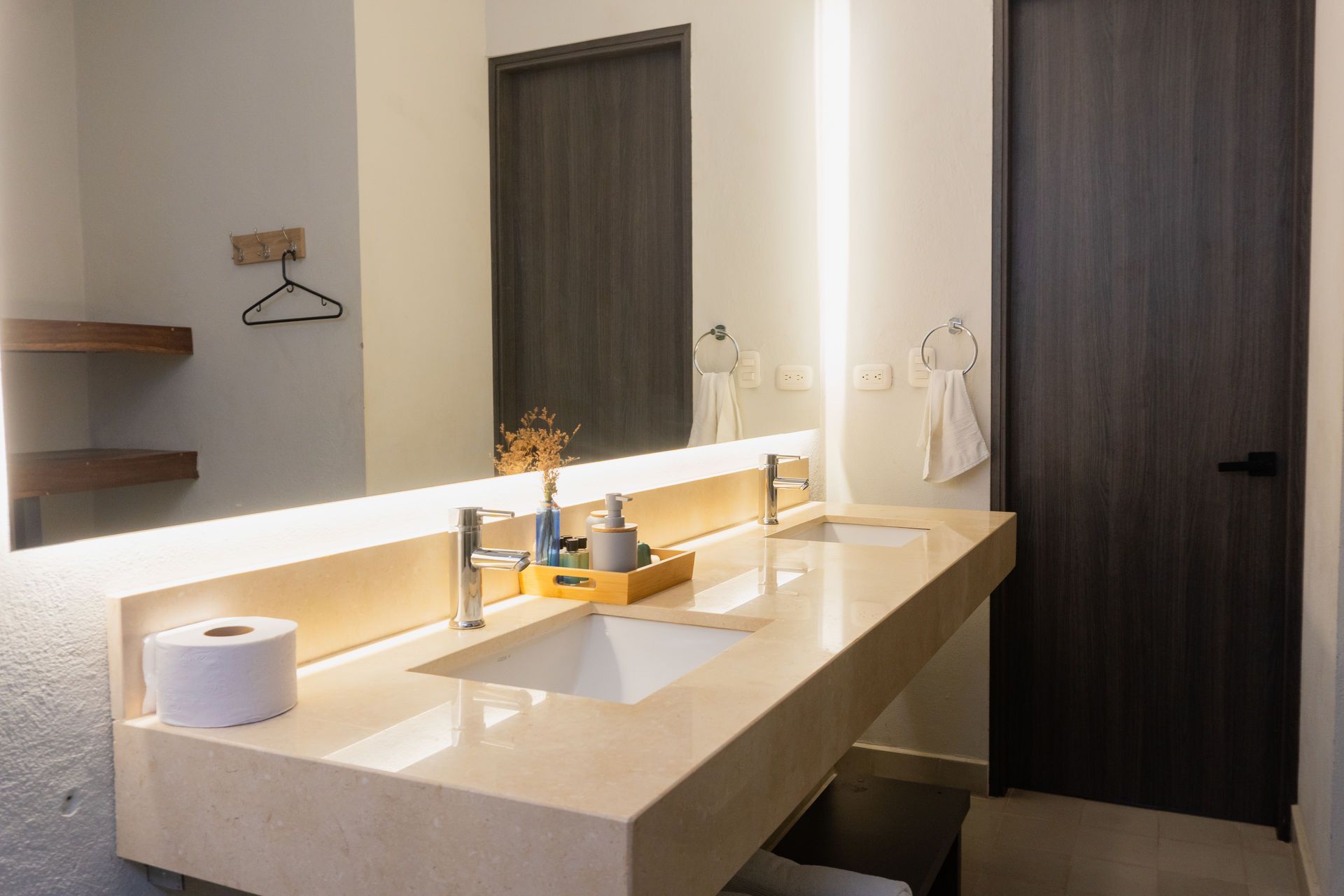 Baño con encimera larga, lavabos dobles, espejo grande y puerta de madera oscura.