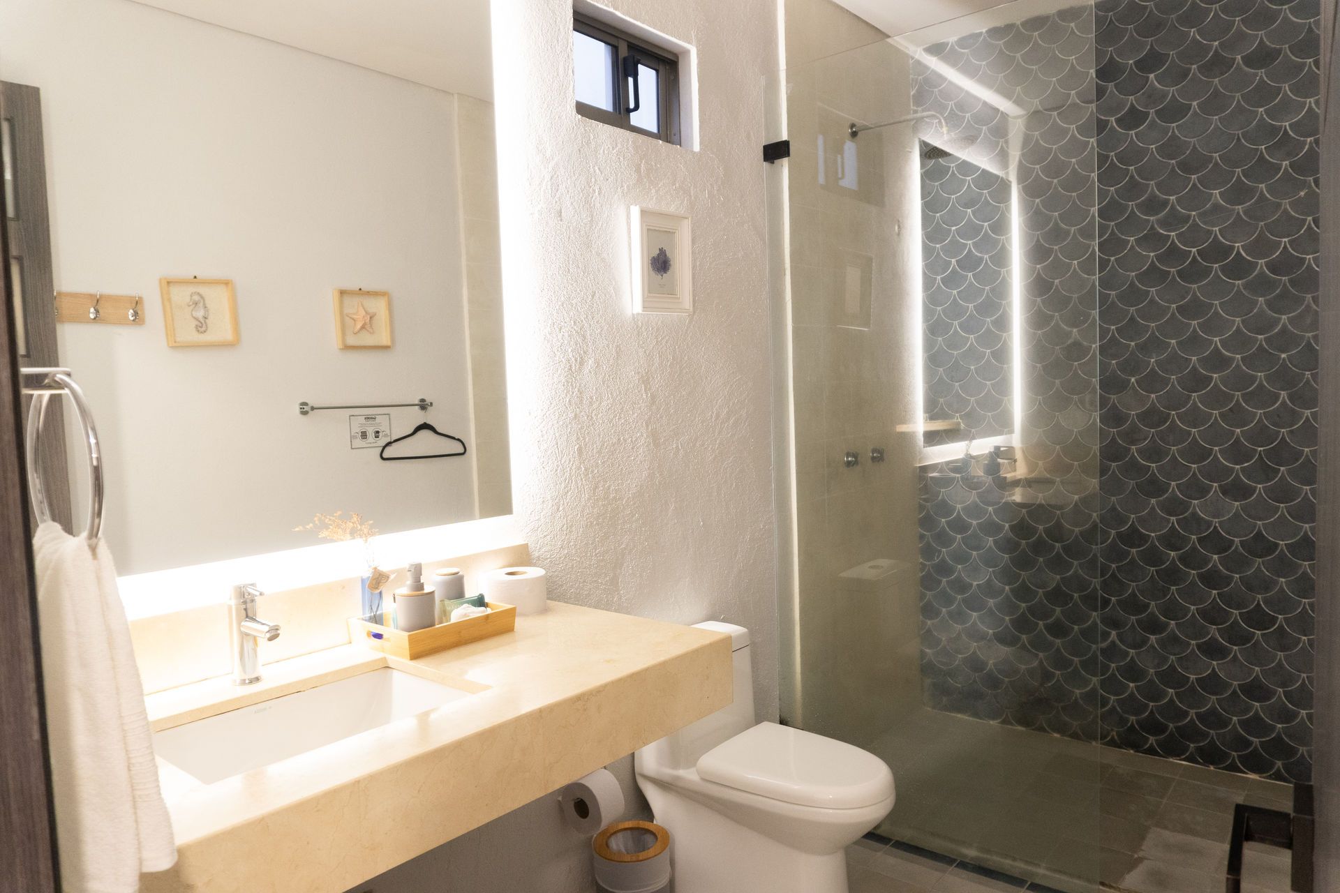 Baño con gran espejo, encimera de piedra, ducha a ras de suelo y sanitario blanco.