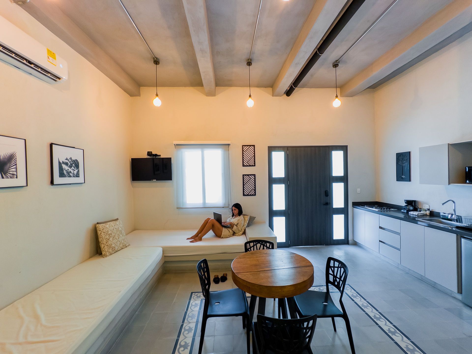 Mujer relajada leyendo en un sofá empotrado. Cocina y comedor visibles en la habitación.