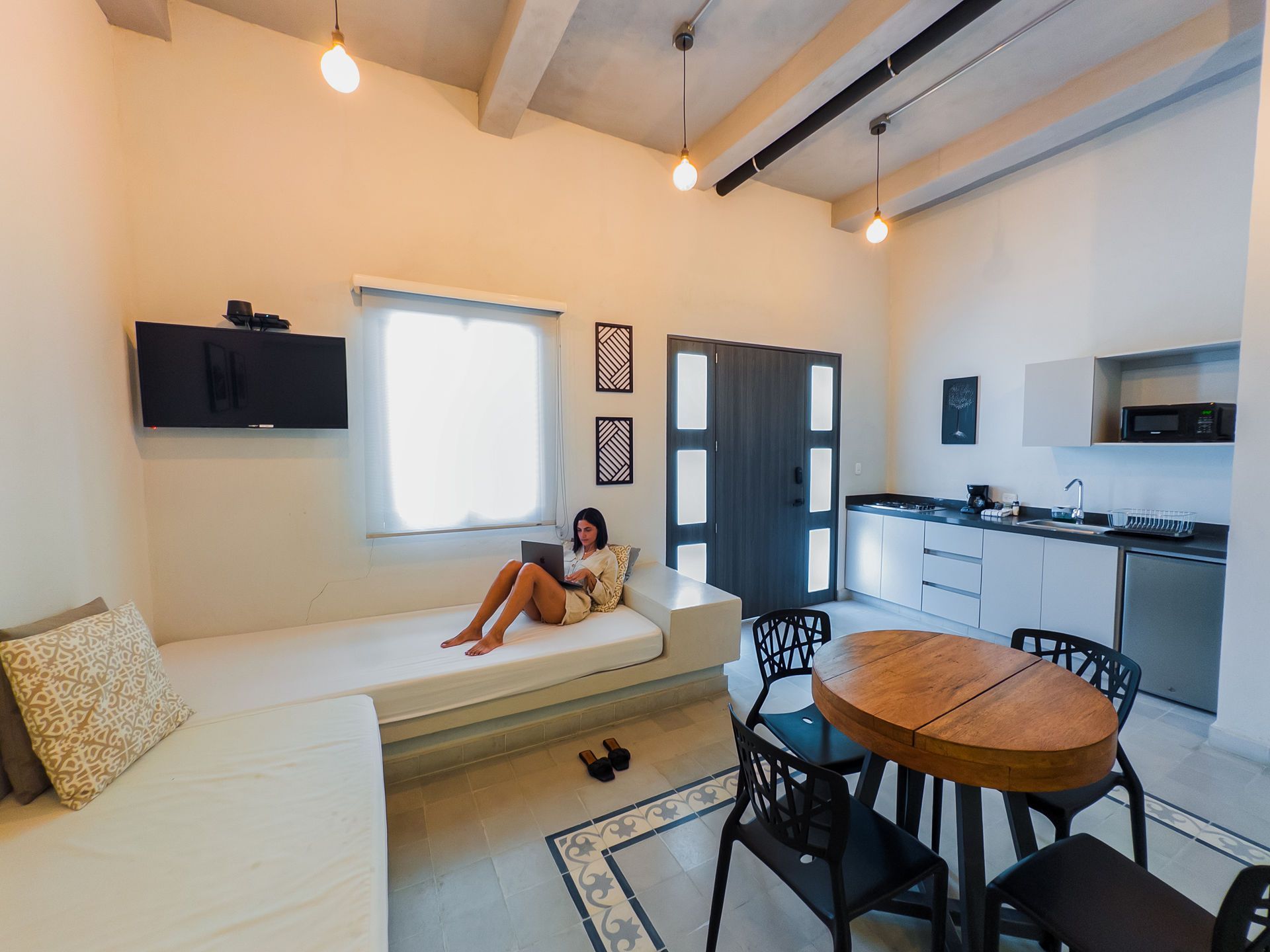 Mujer usando una computadora portátil en un sofá en un apartamento moderno, cerca de una mesa de comedor y una cocina.