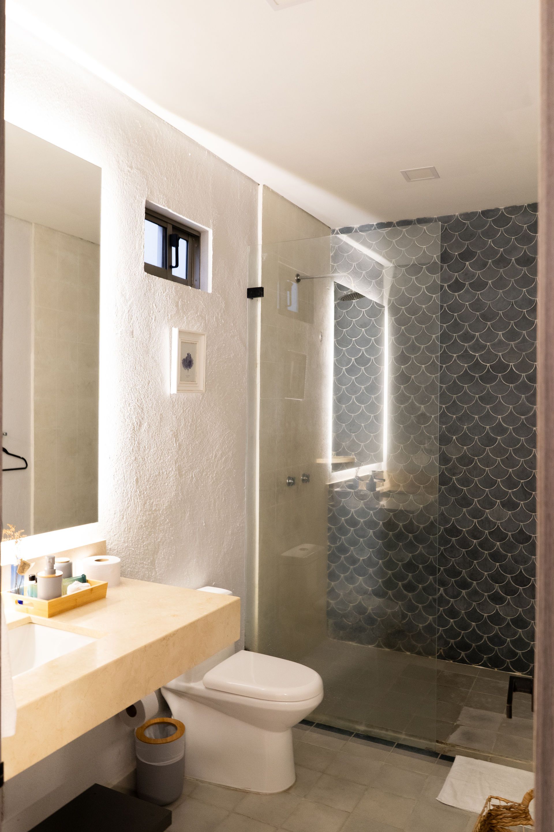 Baño moderno con tocador y paredes de colores claros, ducha de vidrio y pared con acento de azulejos oscuros estampados.